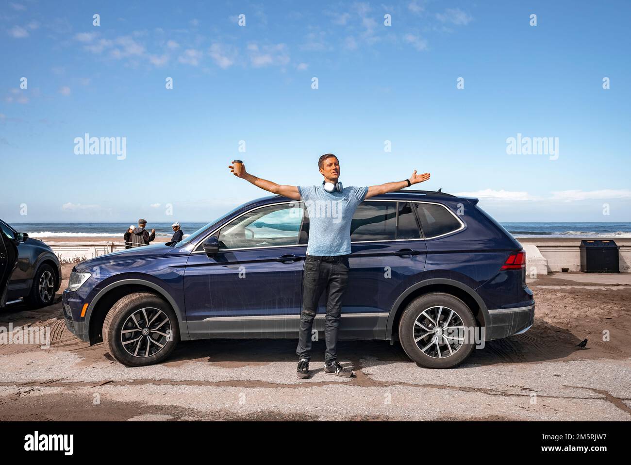 Carefree man with arms outstretched standing by car at beach during summer Stock Photo
