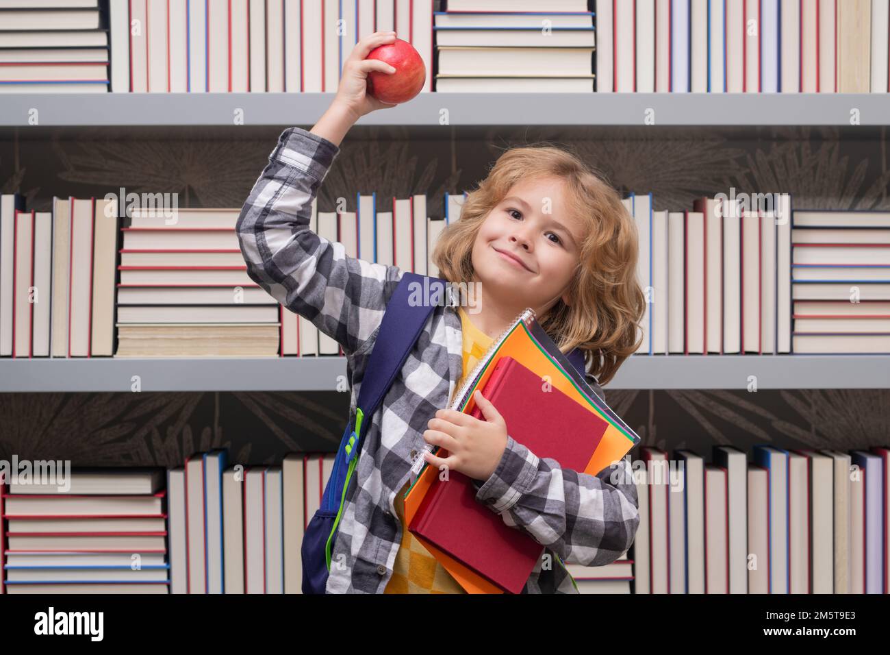 School boy with books and apple in library. School child. Kid boy from elementary school. Pupil go study. Clever schoolboy learning. Kids study Stock Photo