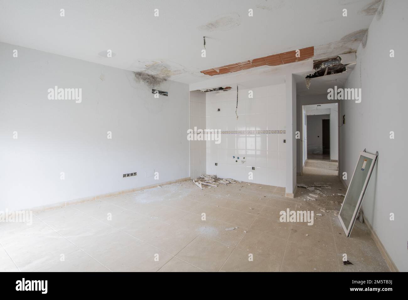 An unfinished empty room with kitchen tiles on one wall and heavy