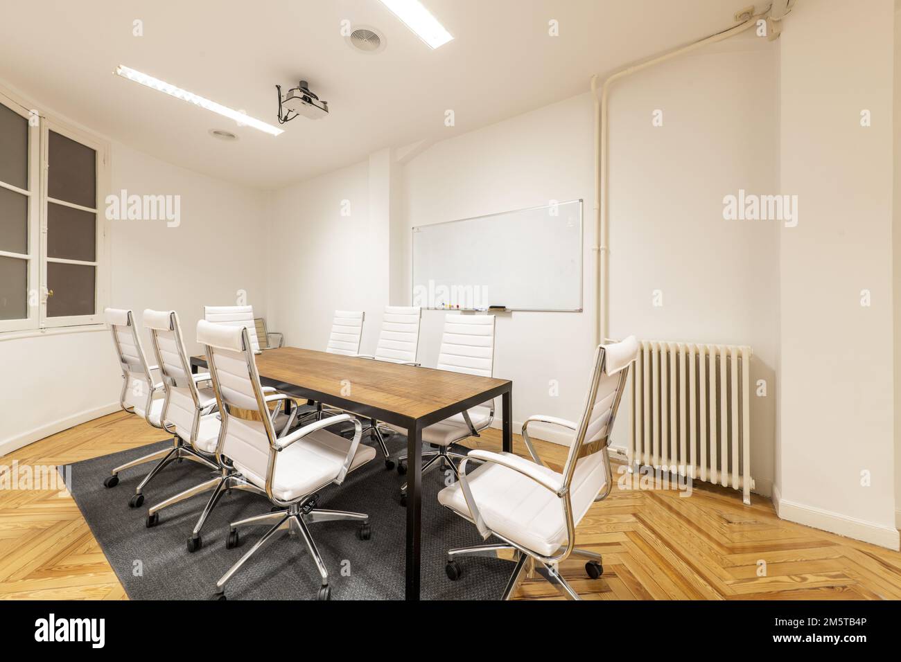 Meeting room with wooden office table with metal frame and swivel chairs upholstered in white skai, whiteboard for erasable markers and projector on t Stock Photo