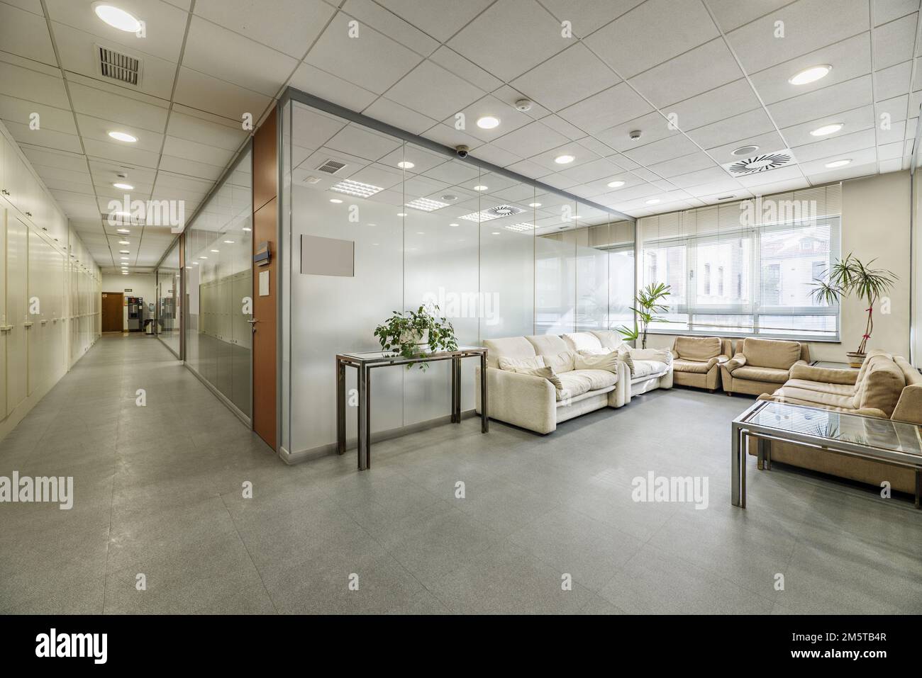 Corridor of an office building and separate offices with glass partitions, waiting areas with sofas and technical ceilings Stock Photo