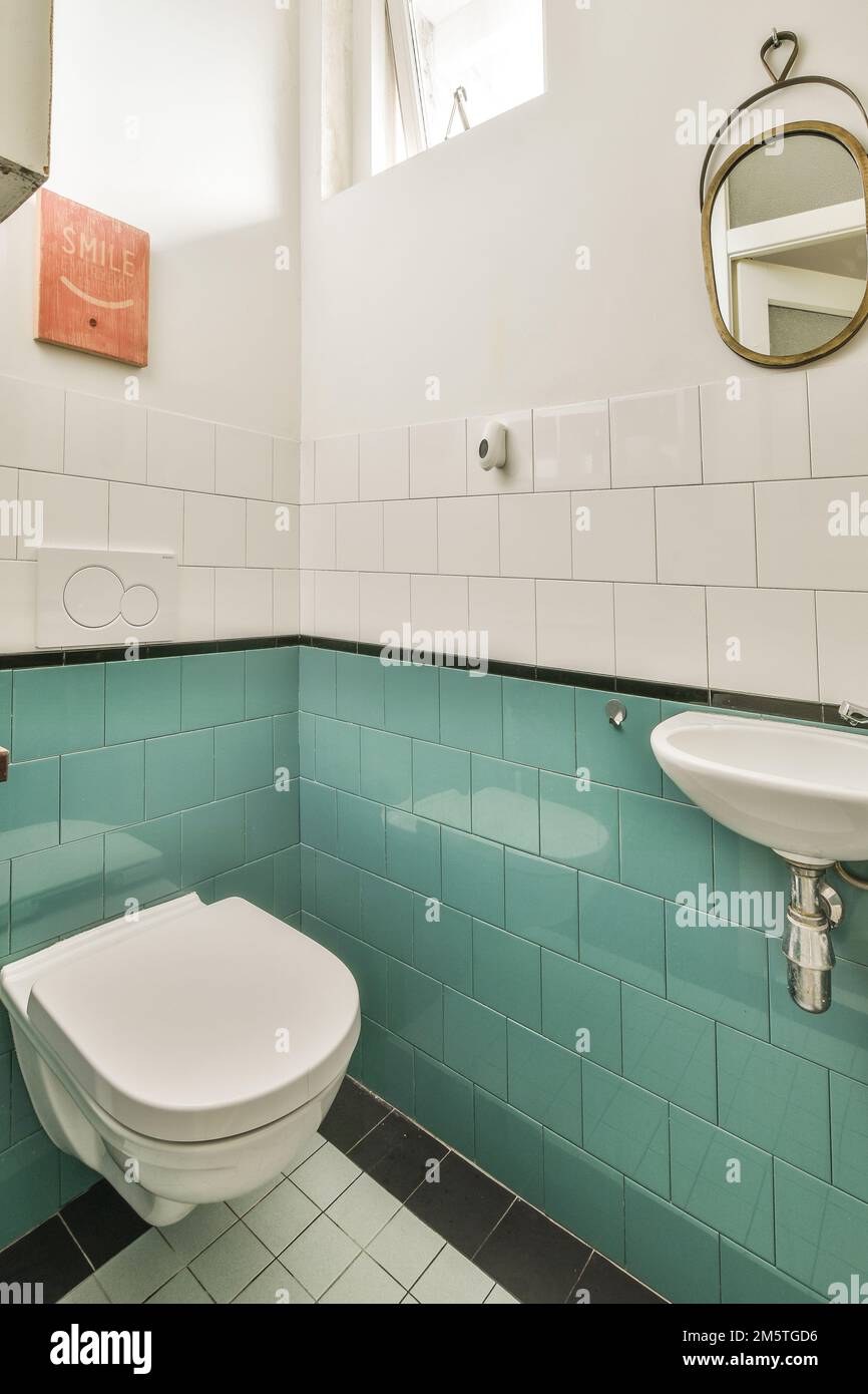 a bathroom with blue tiles on the walls and white fixtures in the toilet bowl is next to the sink basin Stock Photo