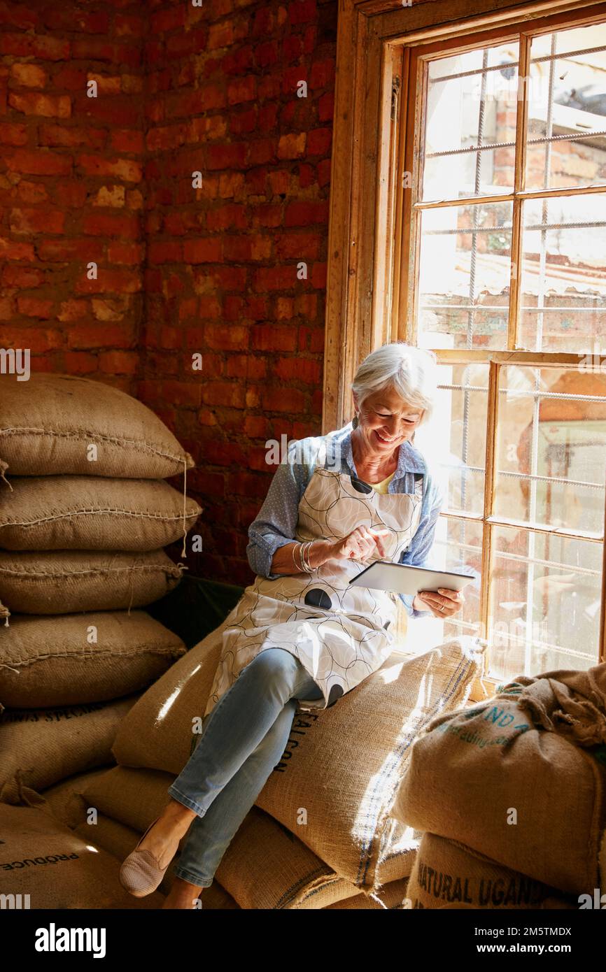 Searching online for exotic coffee beans. a senior woman using a tablet while working in a roastery. Stock Photo