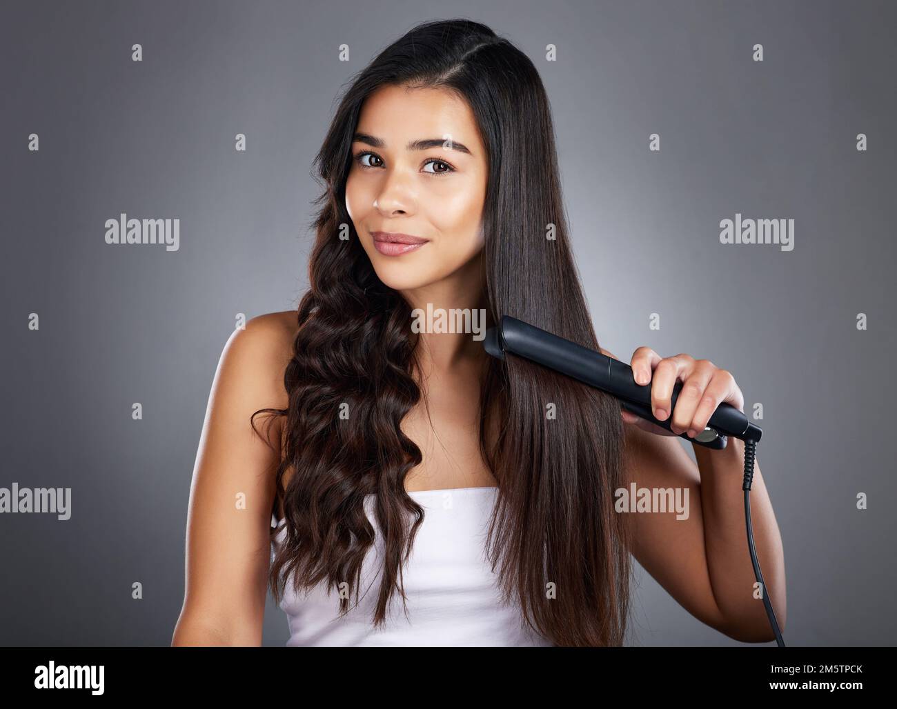 Portrait, woman and hair straightener for care, natural beauty or treatment on grey studio background. Female, girl and salon equipment for luxury Stock Photo