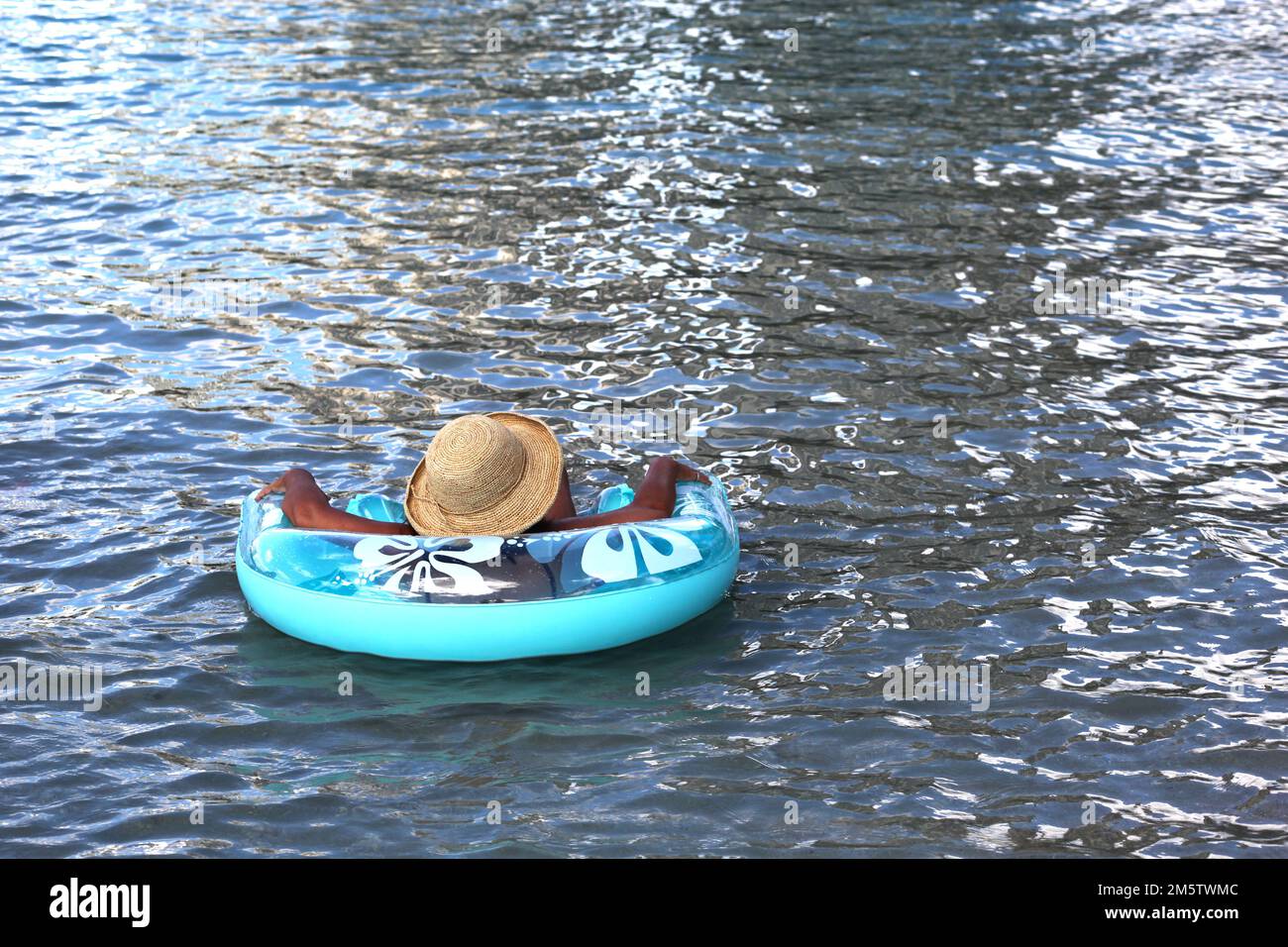 Tan woman covered my straw sunhat relaxing on inflatable tube float in the sea, lake, river or pool Stock Photo
