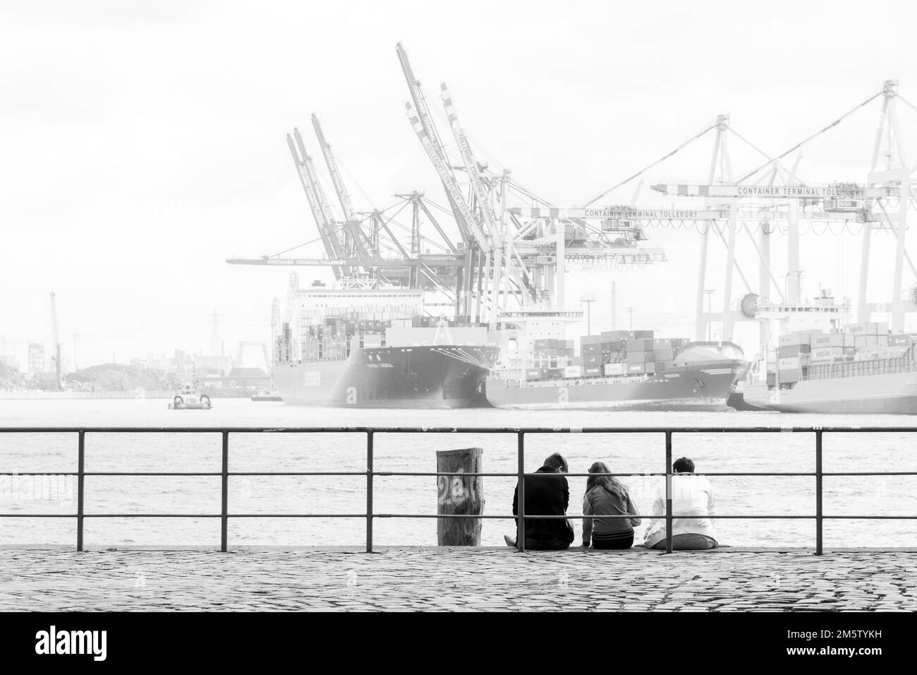Three people sitting on the quay at the Port of Hamburg, Germany Stock Photo