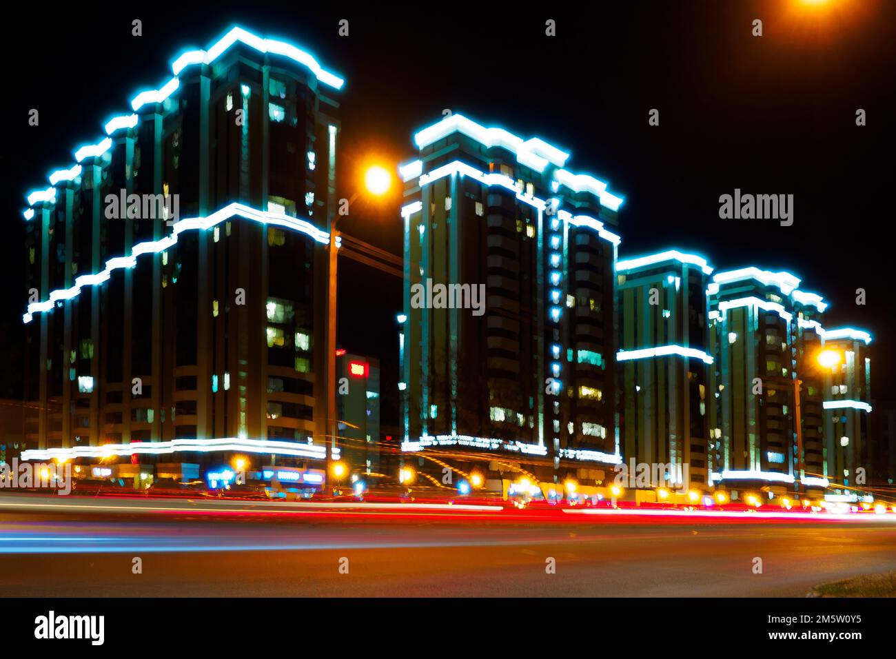 Night city. Photo with motion blur effect. Modern residential multi-storey house with illumination. urban infrastructure. Glow-in-the-Dark Luxury Residential Complex Beautiful Background.. Stock Photo