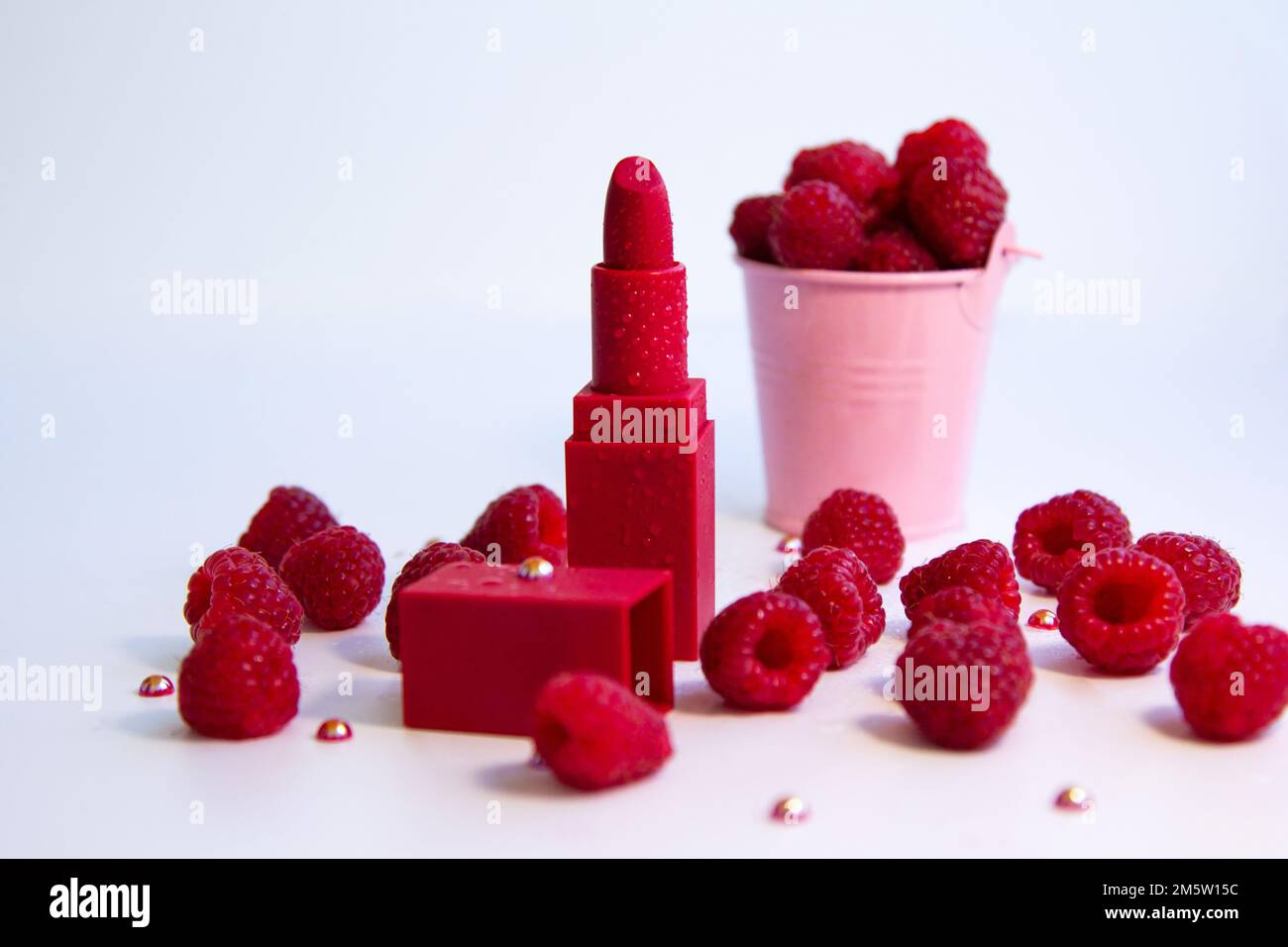 Bright red lipstick and ripe juicy raspberries on white background. Stock Photo