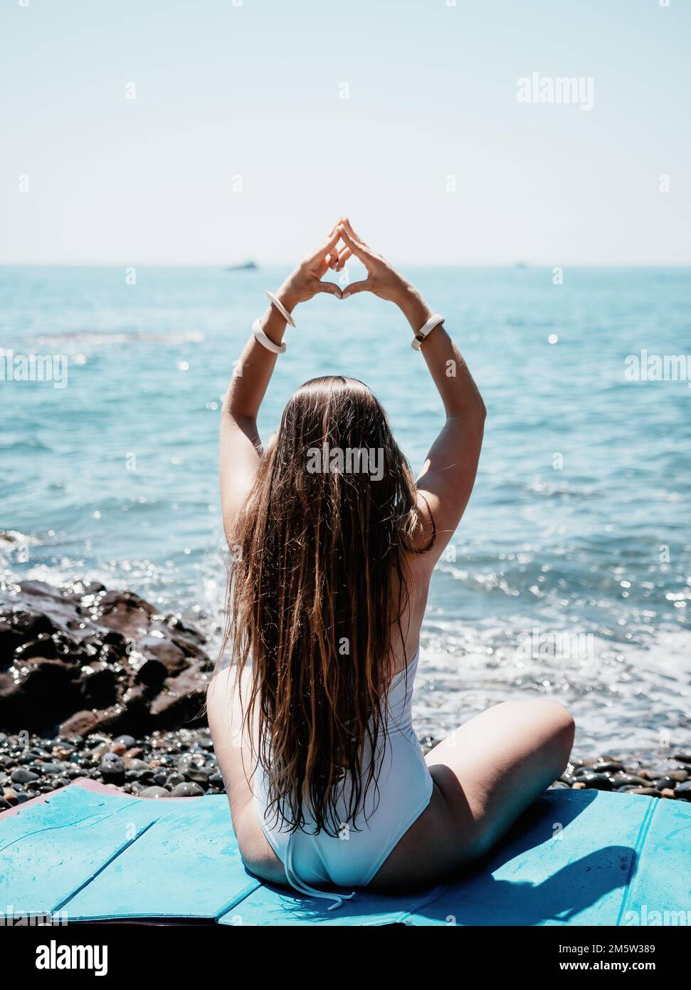 Woman makes heart with hands on beach. Young woman with long hair in ...