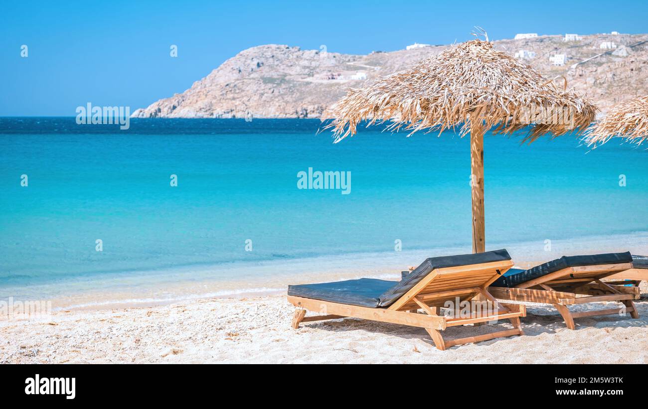 Mykonos beach during summer with umbrella and luxury beach chairs beds, blue ocean with a mountain at Elia beach Mikonos Greece beach Stock Photo