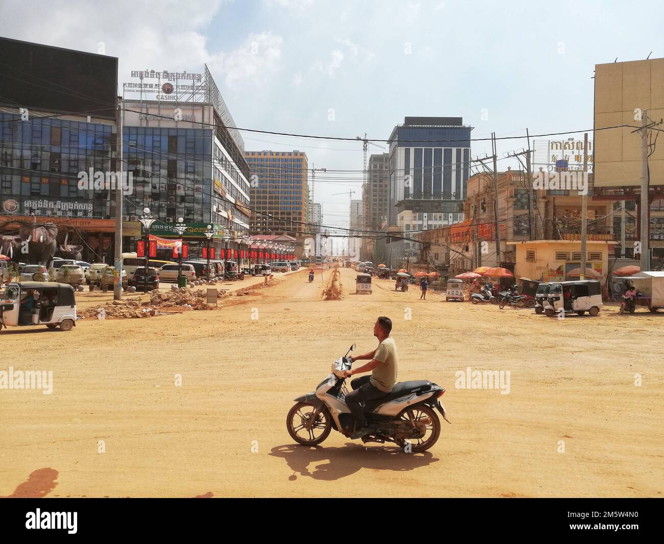 A man on a scooter driving through the dusty city of Sihanoukville in Cambodia Stock Photo