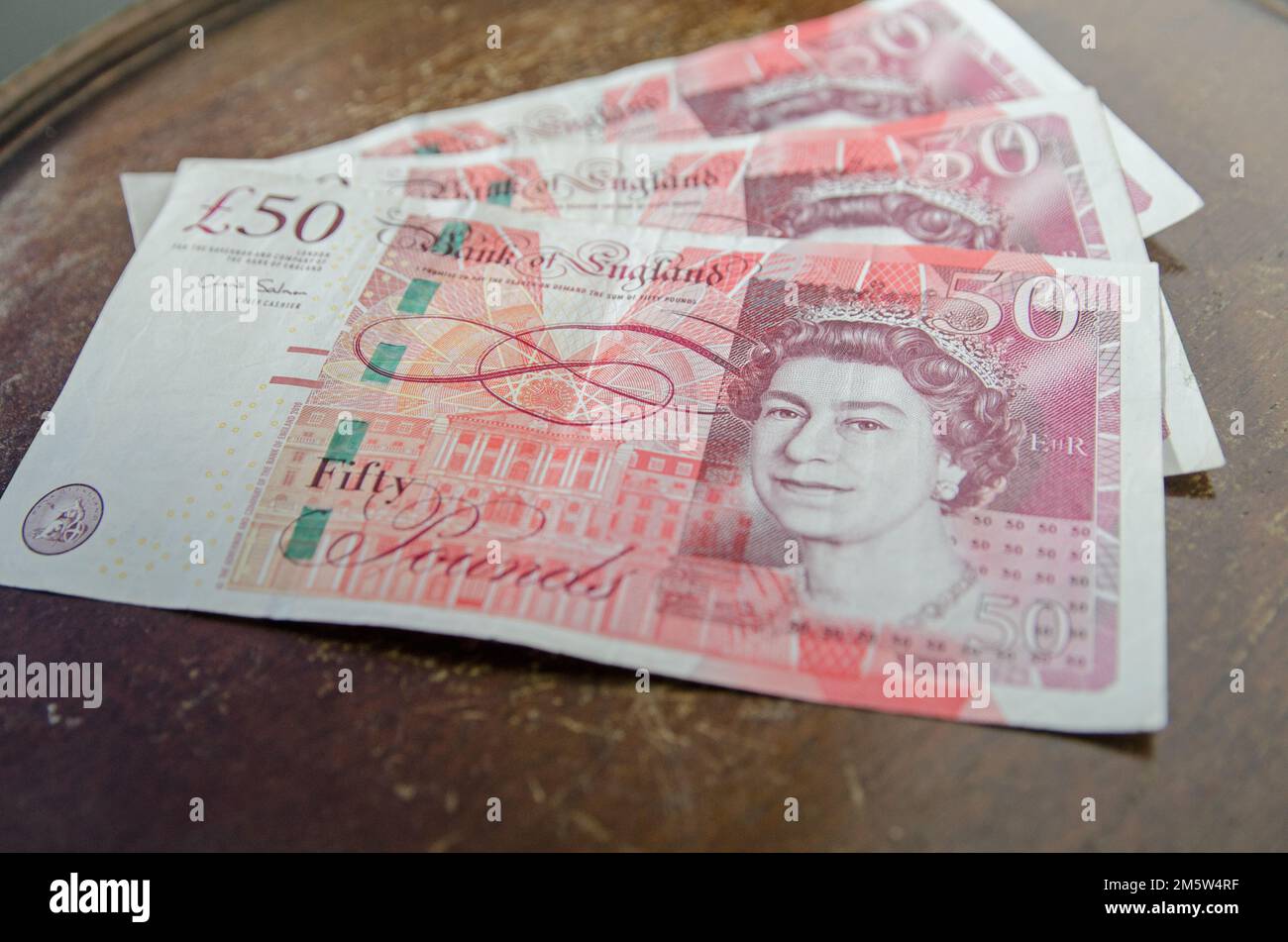A fan of three £50 banknotes from the Bank of England showing Queen Elizabeth II in a pink and orange print.  Used banknotes, photographed at an angle Stock Photo