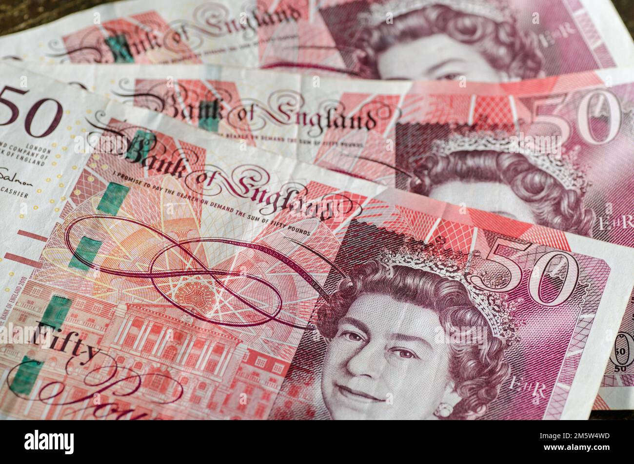 Close up of a fan of three £50 Bank of England banknotes showing Queen Elizabeth II with a pink and orange background.  Used banknotes, photographed a Stock Photo