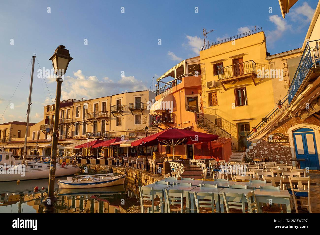 Morning light, sunrise, Venetian harbour, row of houses, colourful houses, taverns, tables, chairs, boats, blue sky, few grey-white clouds Stock Photo