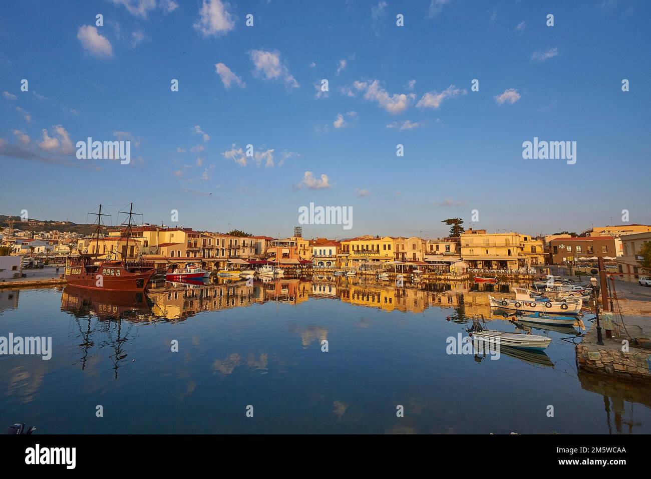 Morning light, sunrise, Venetian harbour, row of houses, colourful houses, reflections in the water, blue sky, few grey-white clouds, Rethimnon Stock Photo