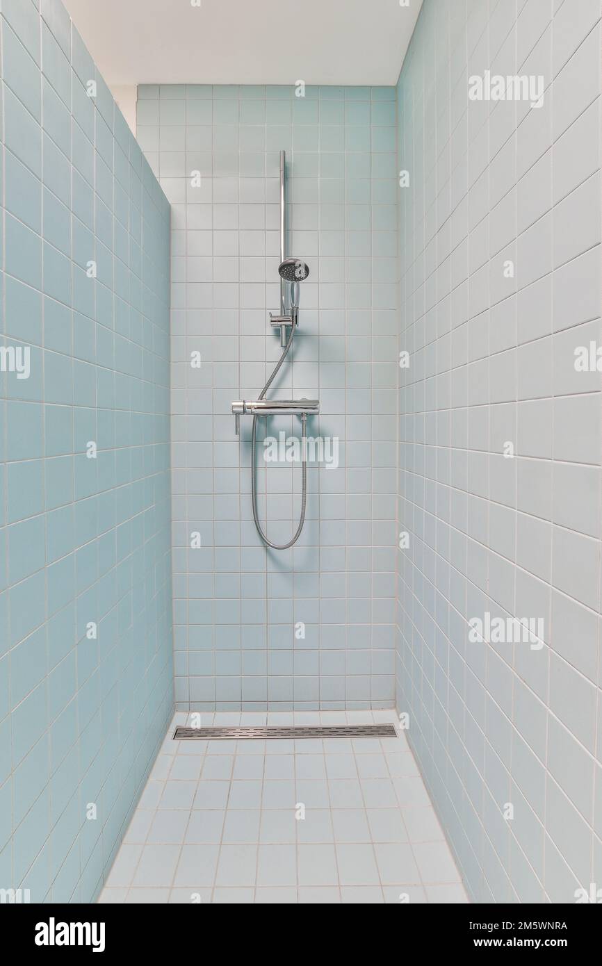 a shower room with blue tiles on the walls and white tile flooring around the bathtub, which is also used as a Stock Photo