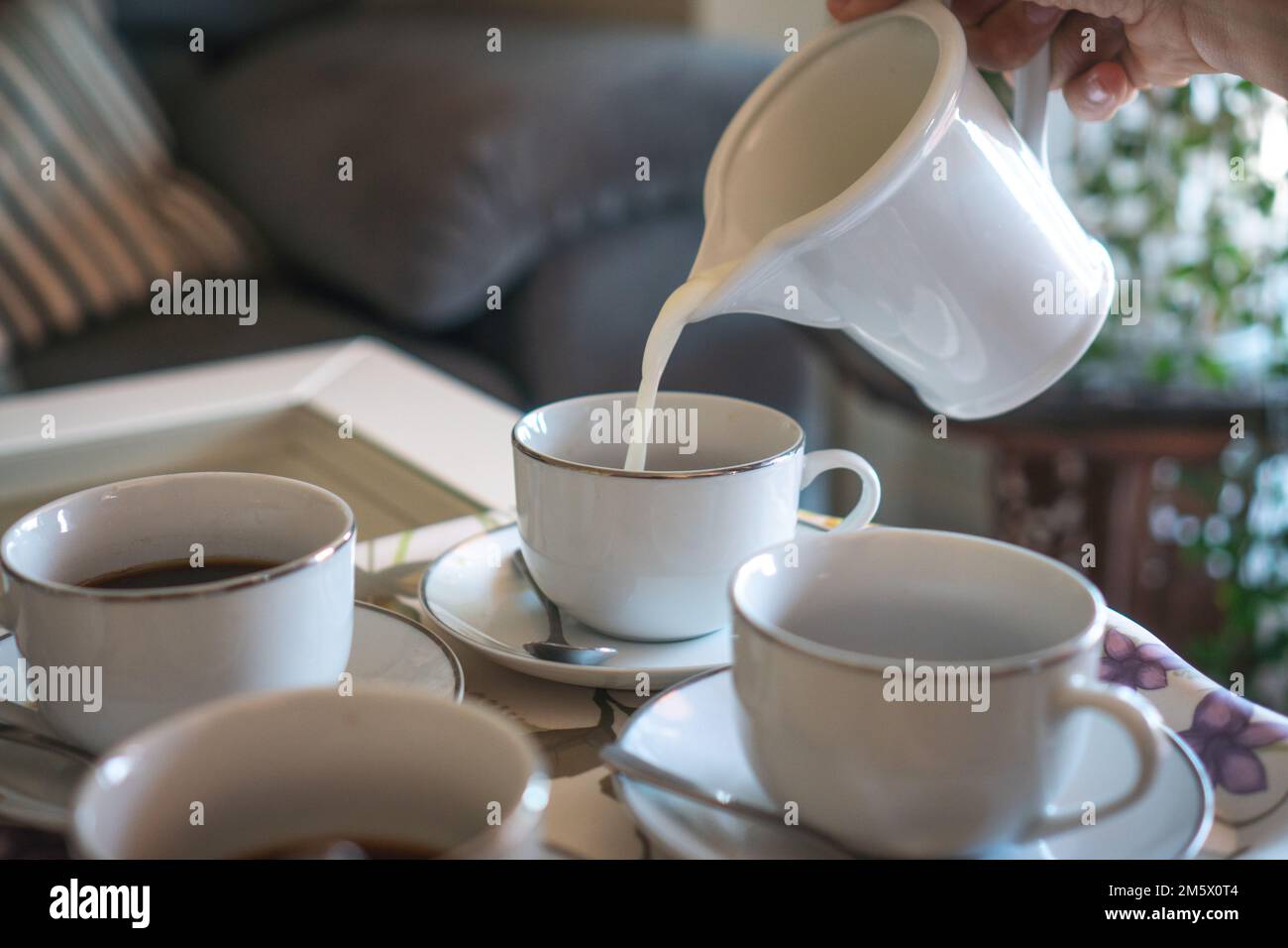 The close-up view of a pitcher pouring milk into white coffee cups Stock Photo