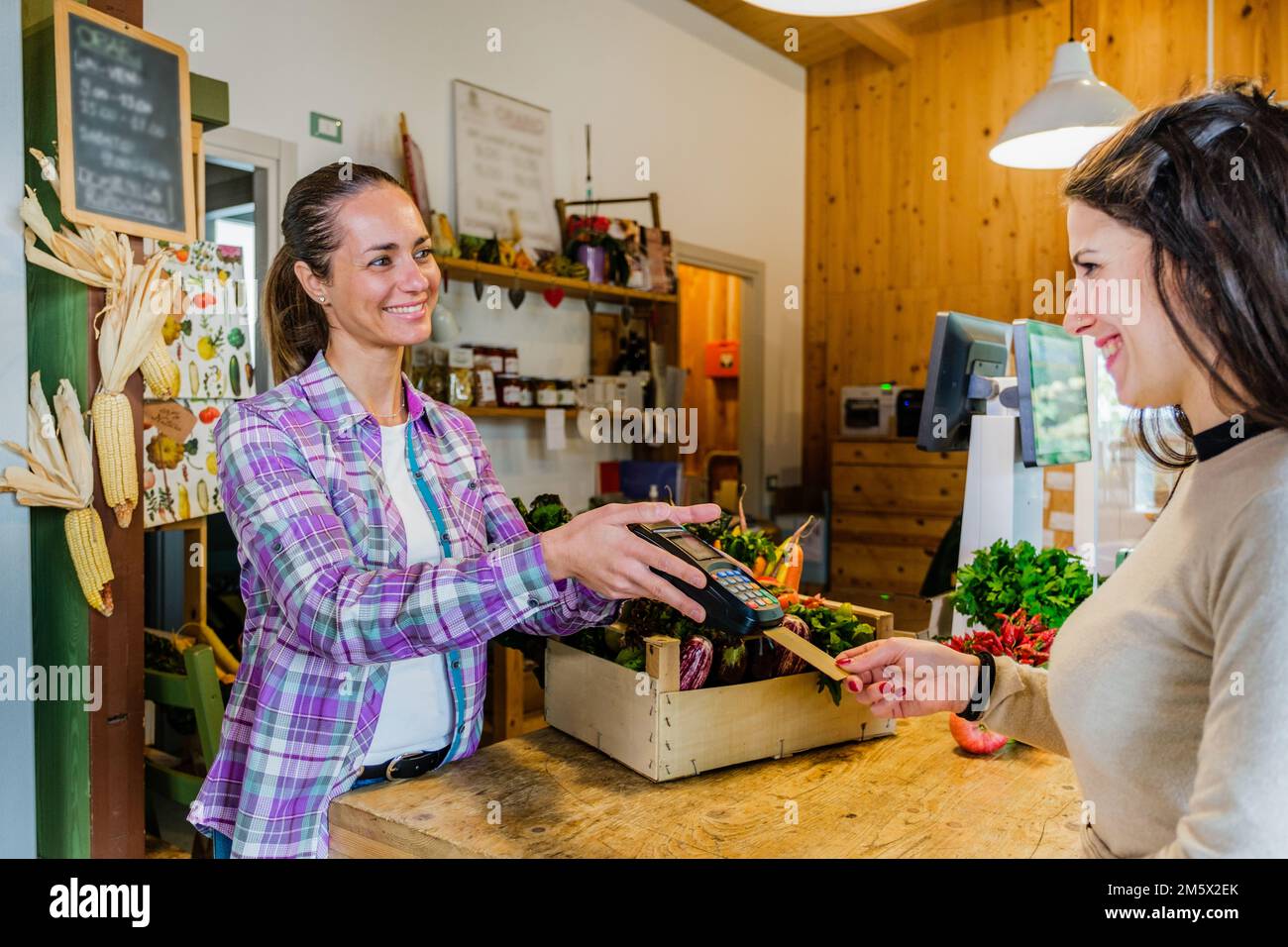 Beautiful customer girl paying for shopping at checkout in a grocery store - Young woman taking a credit card from a customer in a biologic market Stock Photo