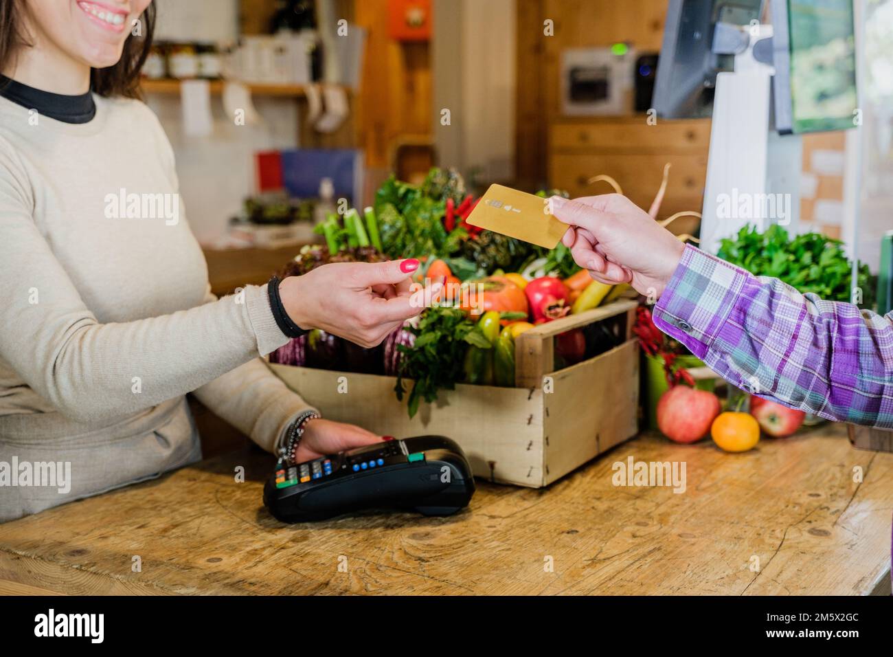 Customer girl paying for shopping at checkout in a grocery store - Young woman taking a credit card from a customer in a biologic market Stock Photo