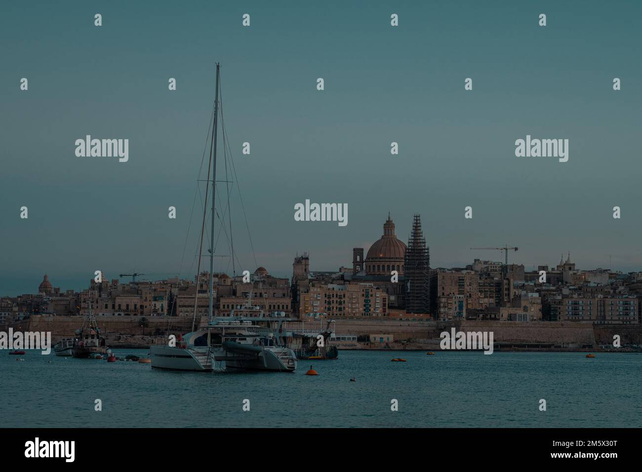 Cityscape of Valletta, Malta on an autumn evening in golden hour or blue hour. Nice panorama with still water and no lights in the city. Stock Photo