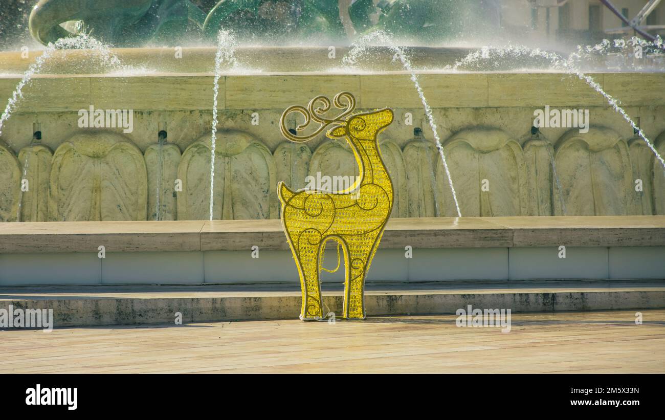Christmas ornament in a shape of a deer in front of a water fountain. Christmas in warm climate. Stock Photo