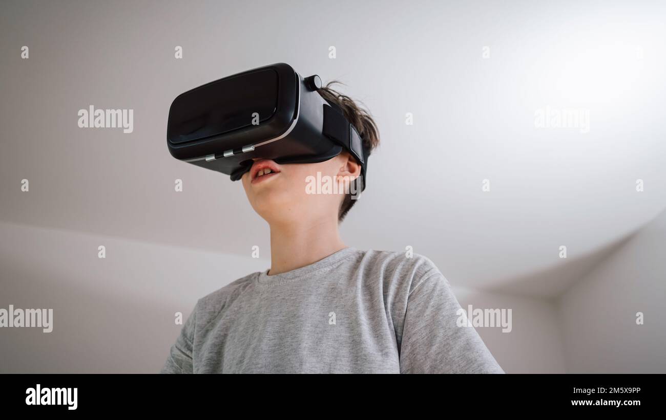 Caucasian male child putting on a virtual reality headset, looking surprised and amazed with a virtual world Stock Photo