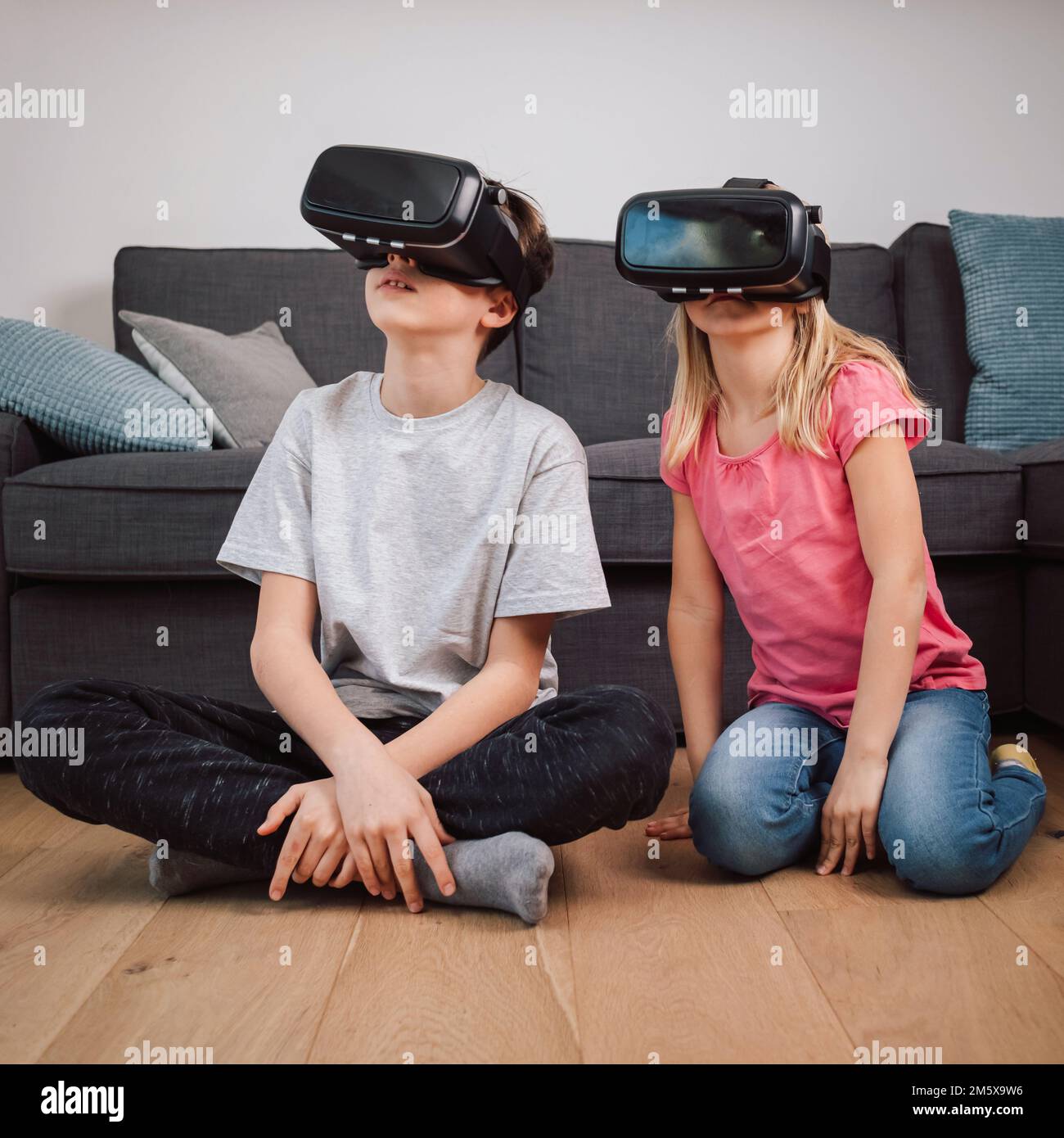 Two Caucasian children, brother, and sister having fun playing at home, using virtual reality headsets Stock Photo