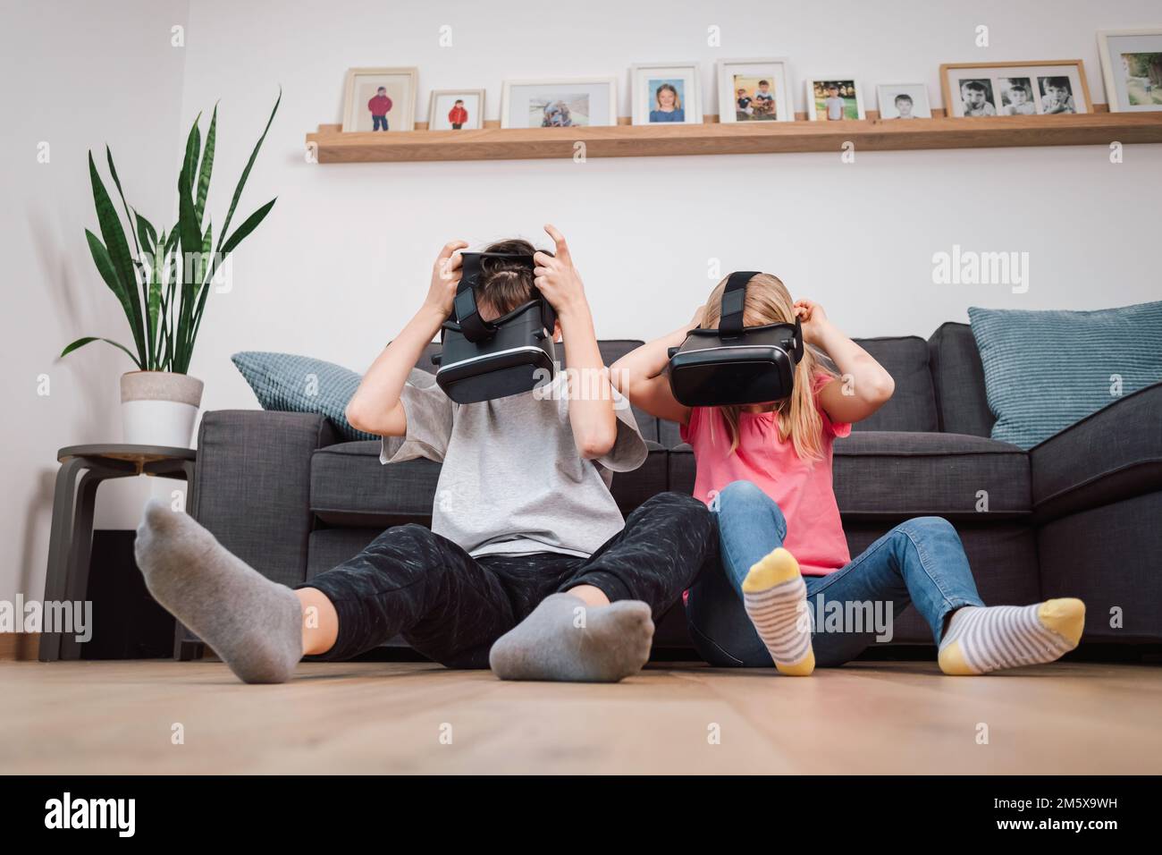 Portrait of two happy smiling children, a boy and a little girl taking off their virtual reality headsets laughing out loud and looking at the camera Stock Photo