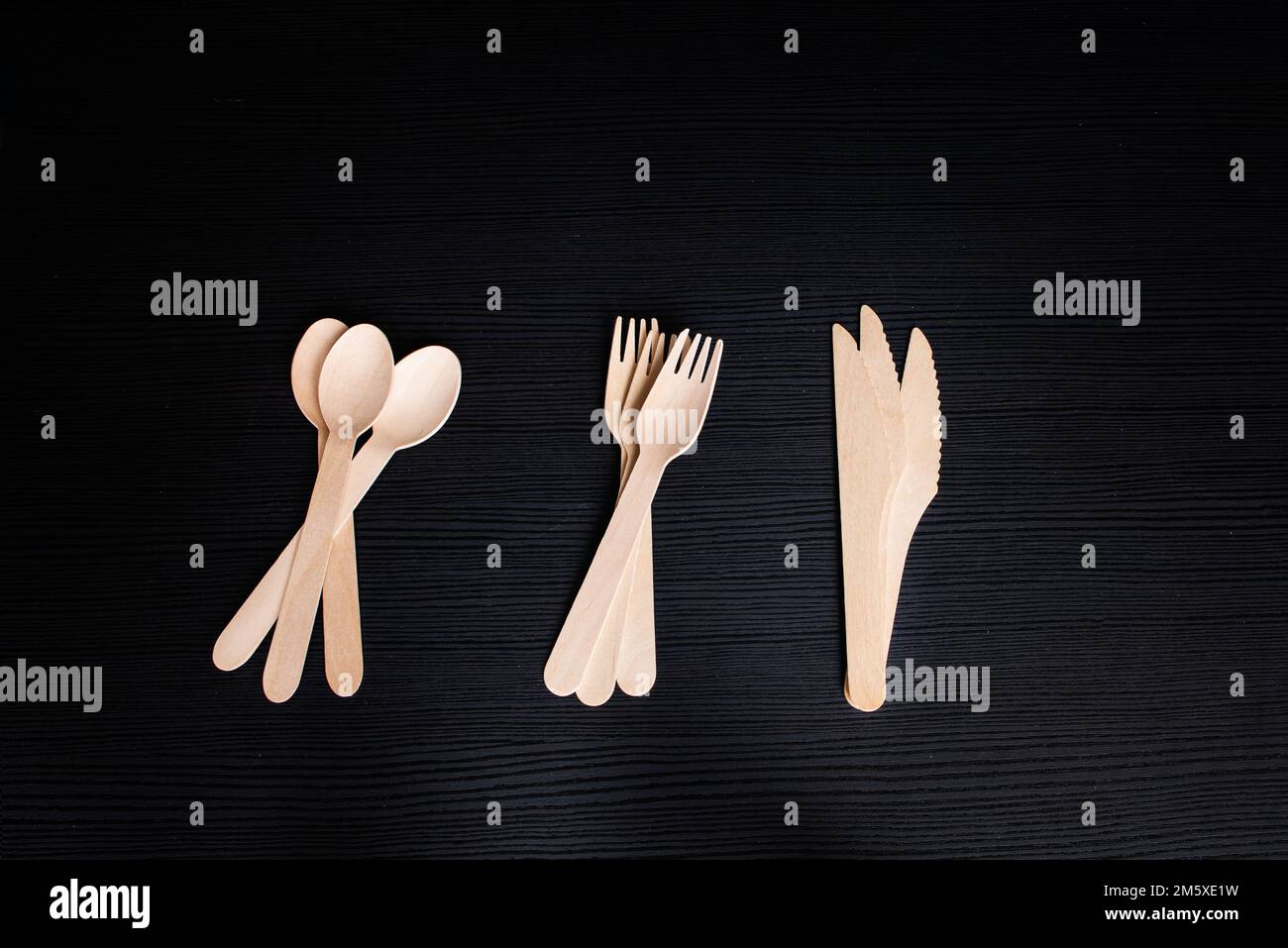 disposable ecofriendly wooden spoons, forks and knives on a dark