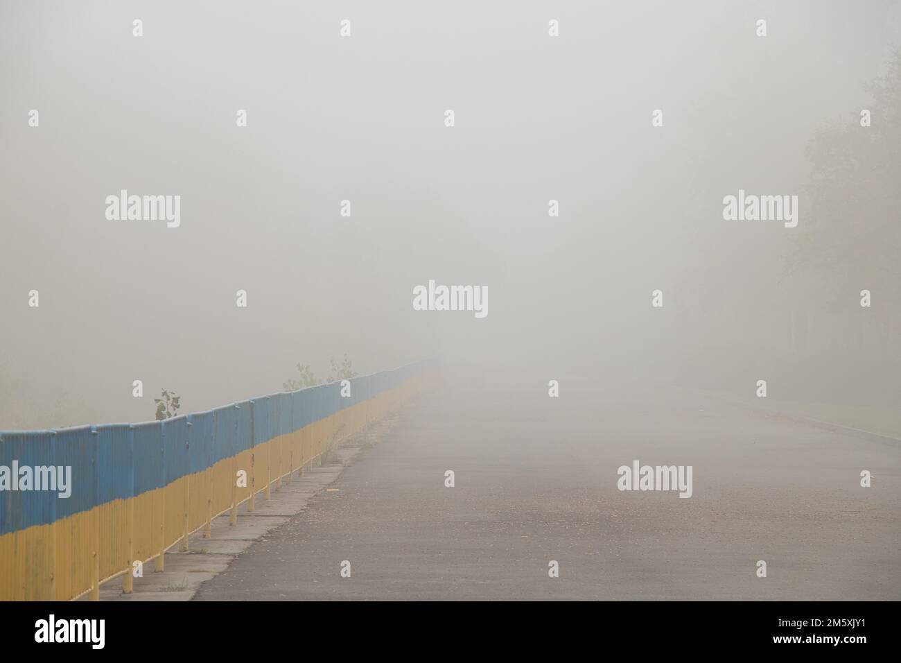 yellow-blue railings along the road in the morning in the fog in Ukraine in the park Stock Photo