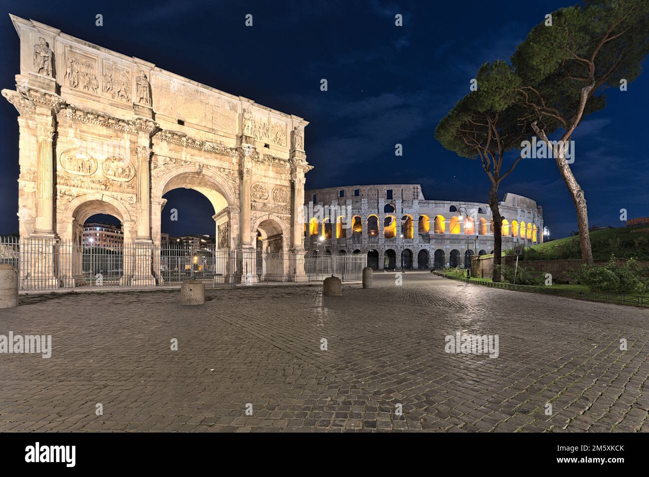 View on the Collosseum and the Arco di Costantino at night time. Only one indistinguishable person is sitting on a bench. Stock Photo