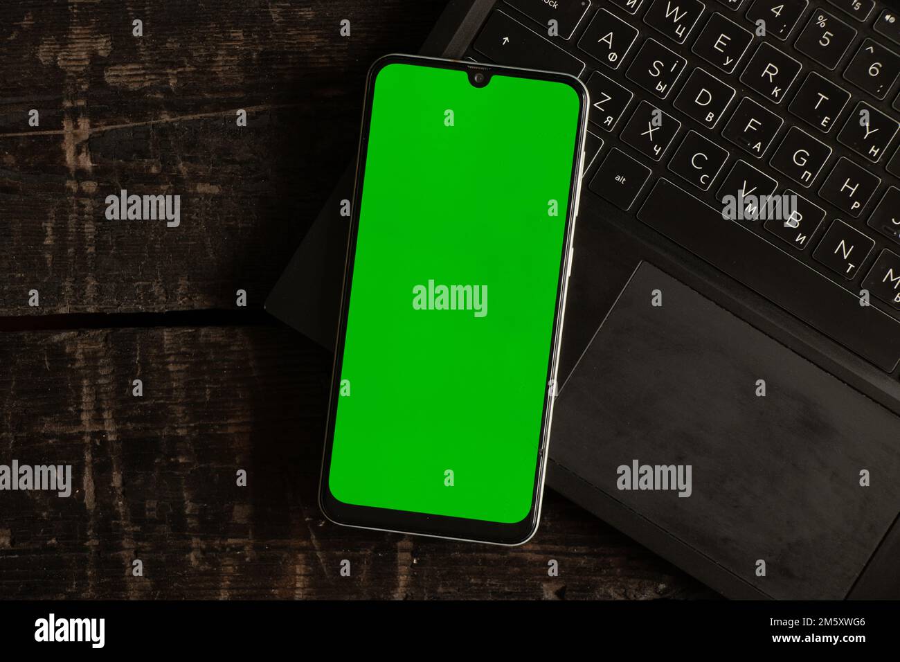 a phone with a green screen lies on a black laptop on a table, a phone template with a green screen Stock Photo