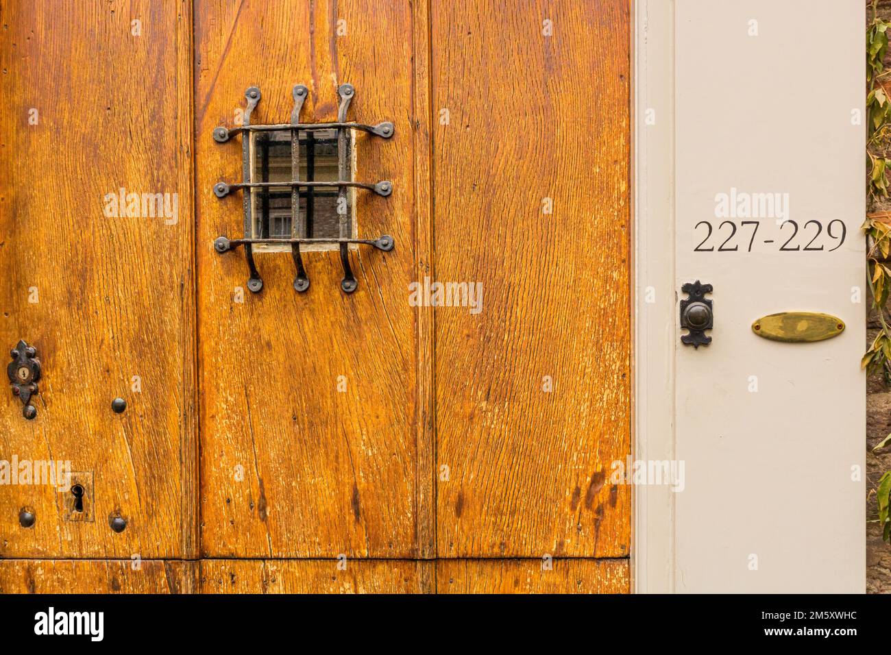 A closeup of peephole, doorbell and house numbers on old wooden front door Stock Photo
