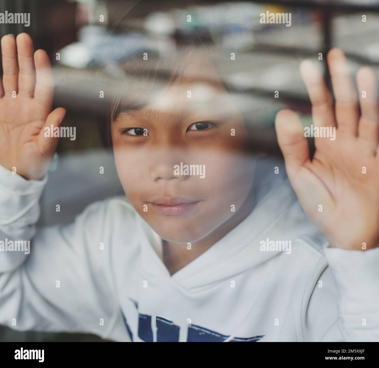 an Asian boy looks through a window with his hands resting on the glass. virus concept and confinement in Asia Stock Photo