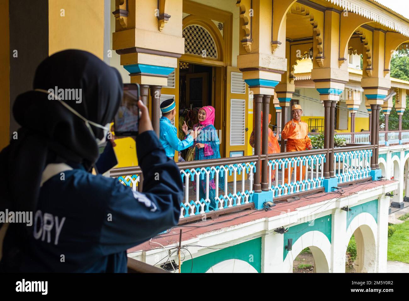 Medan, Indonesia - July 21, 2022: Four actors performing in traditional clothings being filmed by one woman dressed modestly. Taken on an overcast day Stock Photo