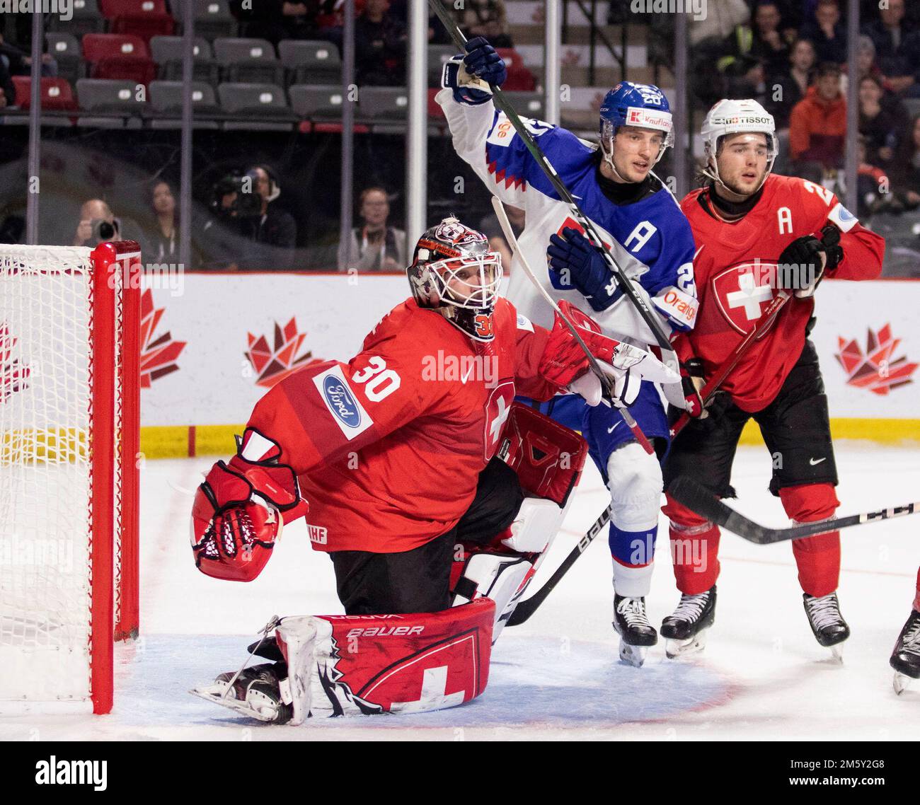 December 31, 2022, Moncton, NB, Canada: Switzerland goaltender Kevin Pasche  tries to keep his balance as Slovakia's Lian Bicsel and Switzerland's Libor  Nemec battle in front of the net during third period