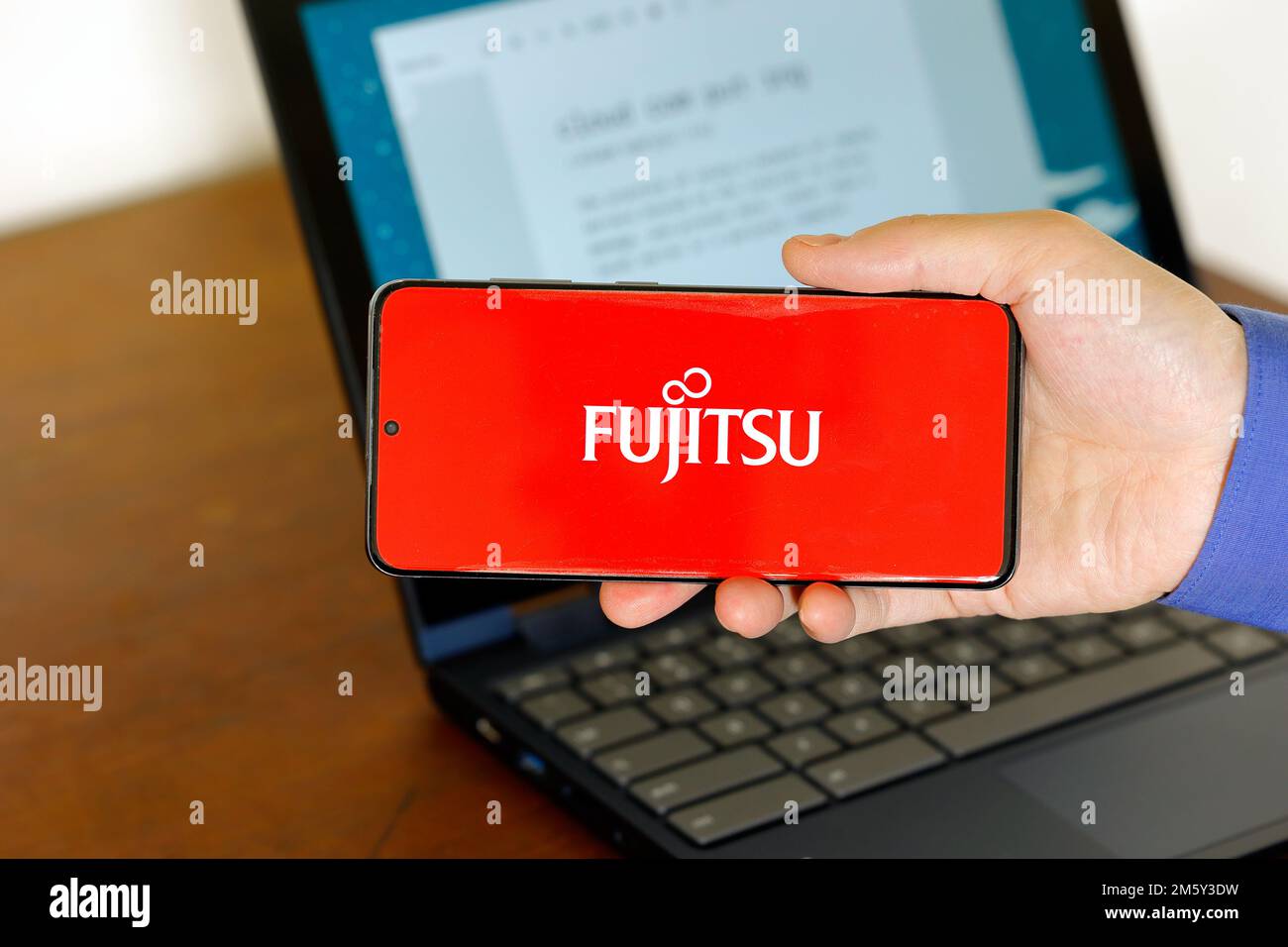 Logo of Fujitsu Cloud on a smartphone in front of a computer. Fujitsu Cloud is cloud computing echnology service from Fujitsu. Stock Photo