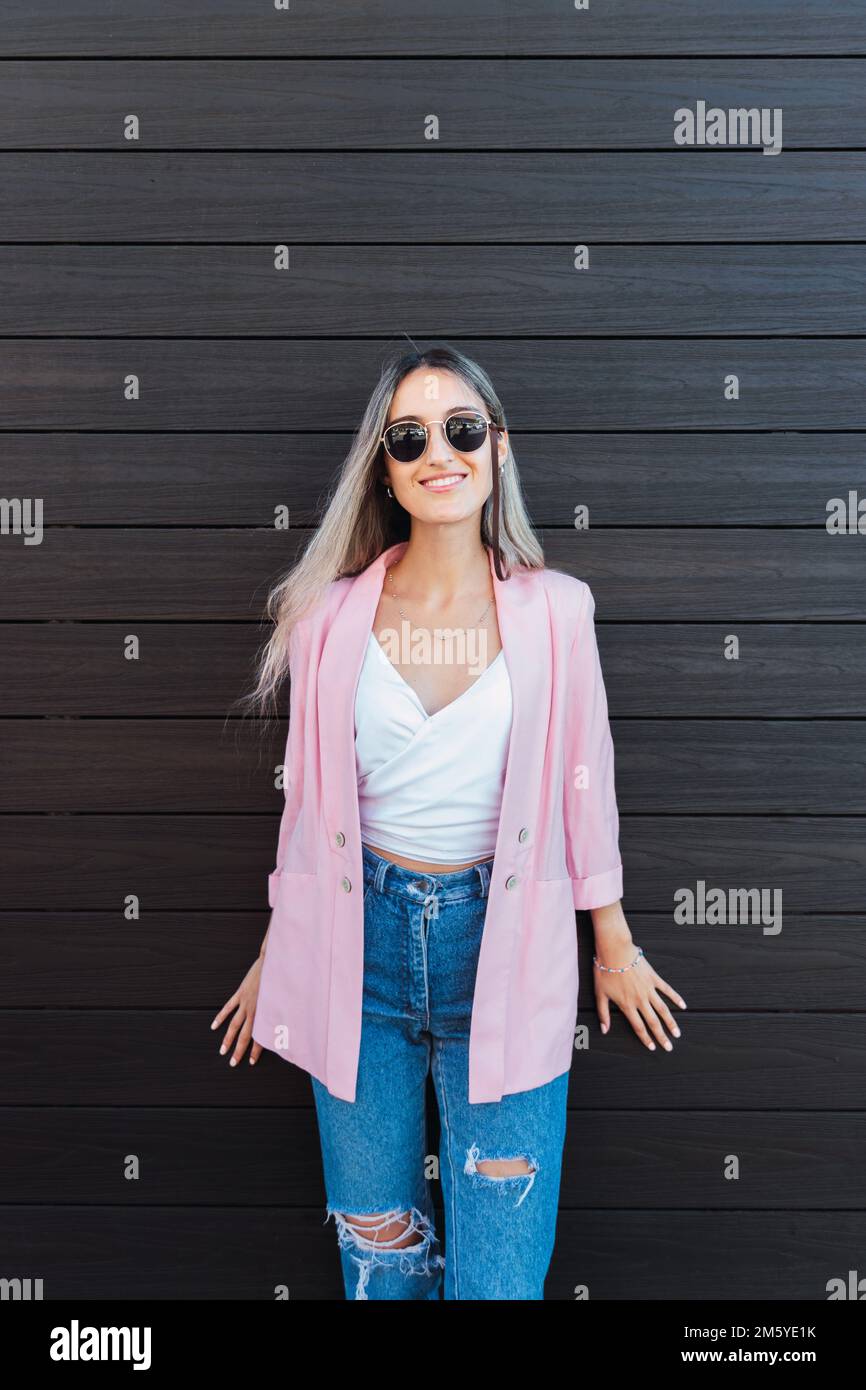 Young smiling blonde woman against a wooden wall leaning with her hands. Feminine empowerment.  Stock Photo