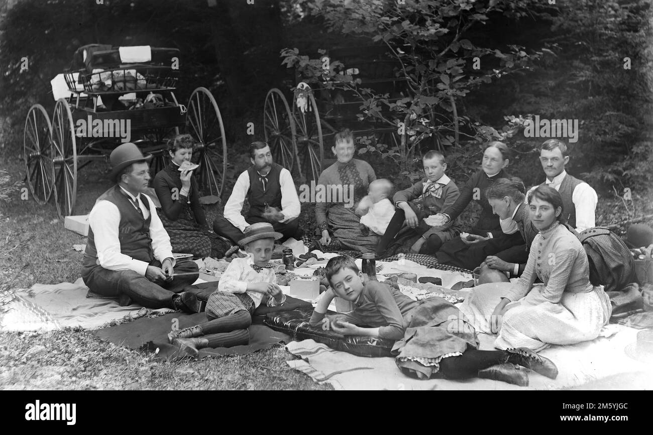 A large family spreads out on a blanket for a picnic Victorian Era style, ca. 1895. Stock Photo