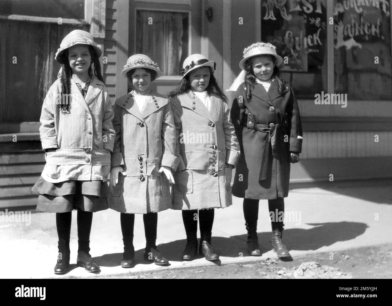 A quartet of young girls in the best Sunday clothes stand in group on a small town America sidewalk, ca. 1930. Stock Photo