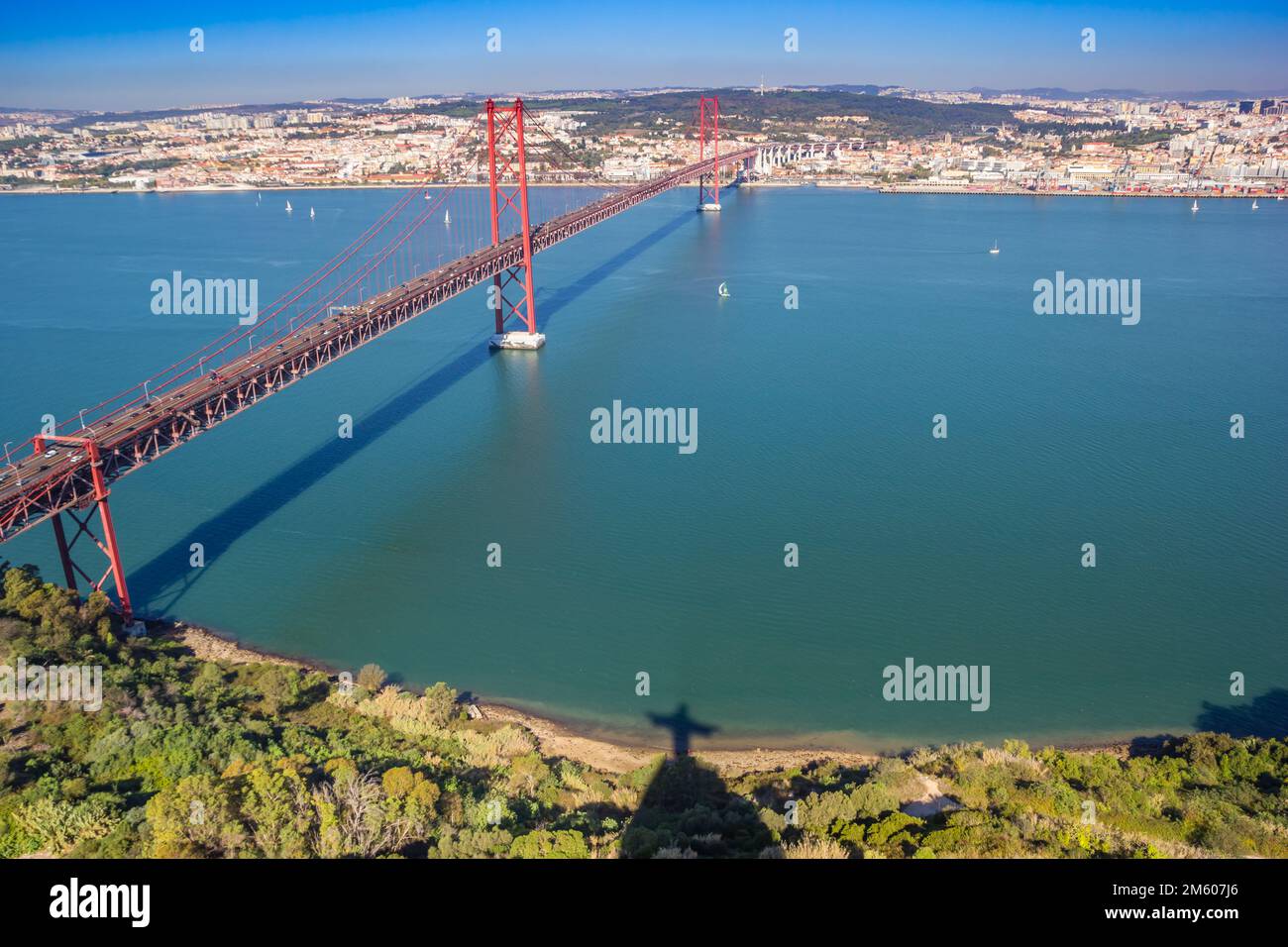 Shadow of the Christ statue in front of the historic red suspension bridge in Lisbon, Portugal Stock Photo