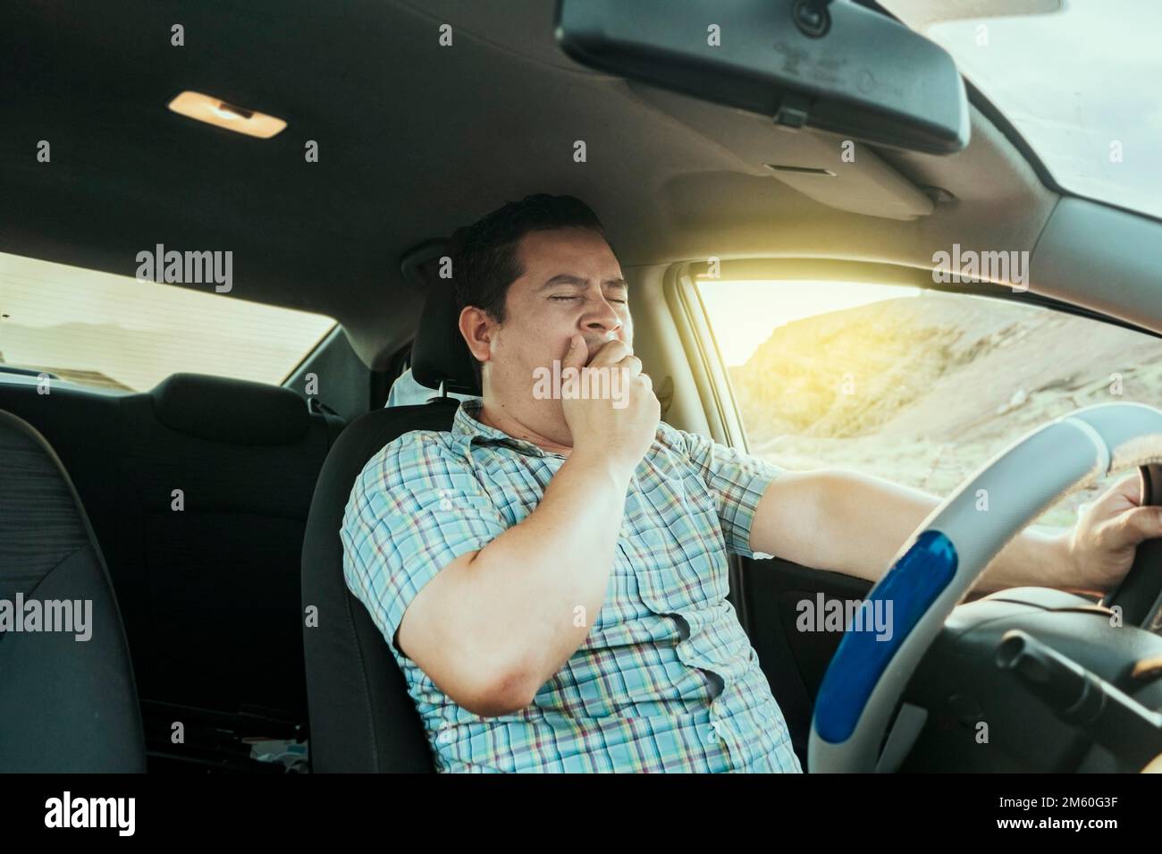 View of a sleepy driver in his car. Tired driver yawning in the car, concept of man yawning while driving. A sleepy driver at the wheel, a tired Stock Photo