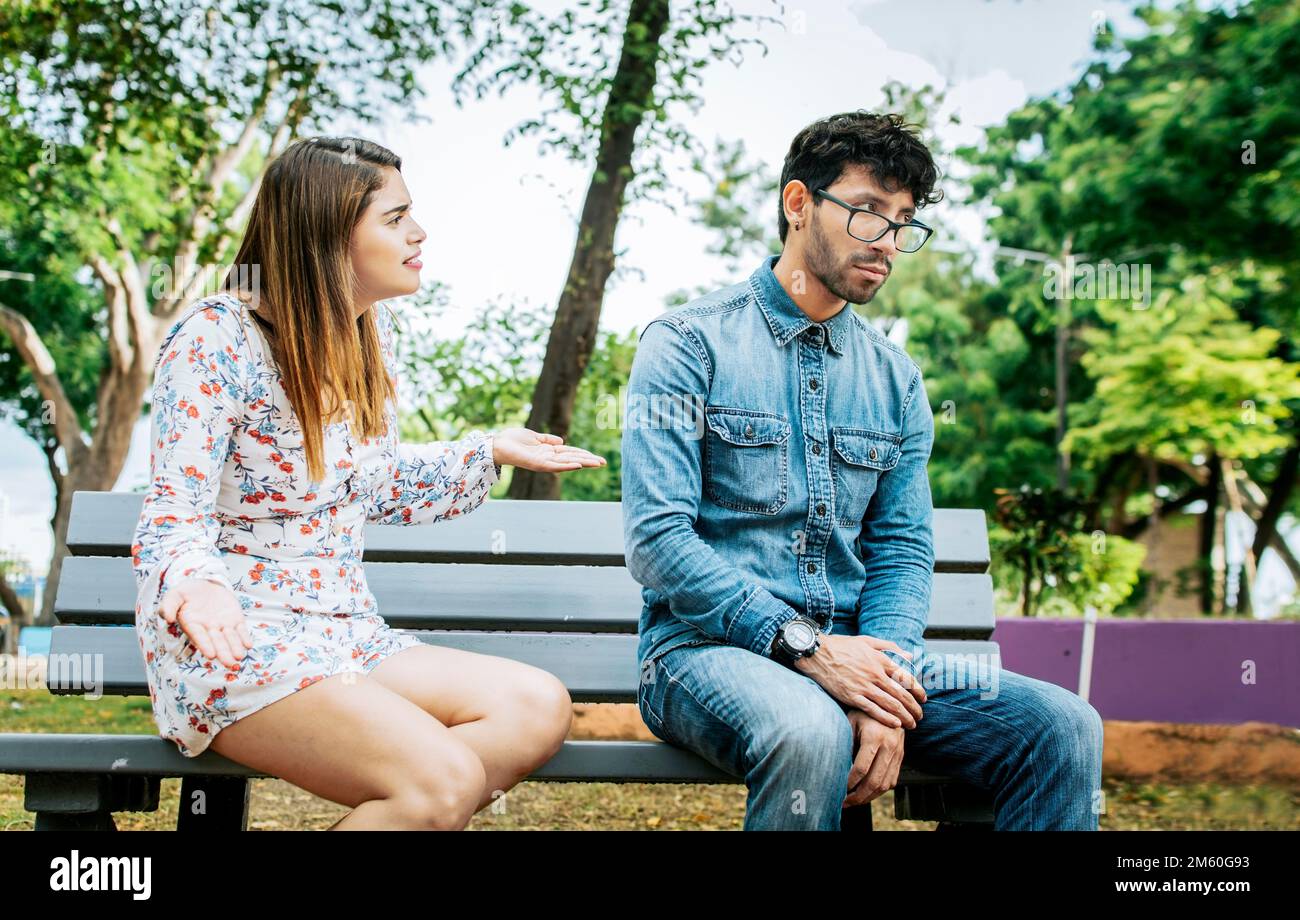 Upset couple arguing in a park. Girl arguing with her boyfriend sitting in a park, Young couple arguing and complaining sitting on a park bench Stock Photo