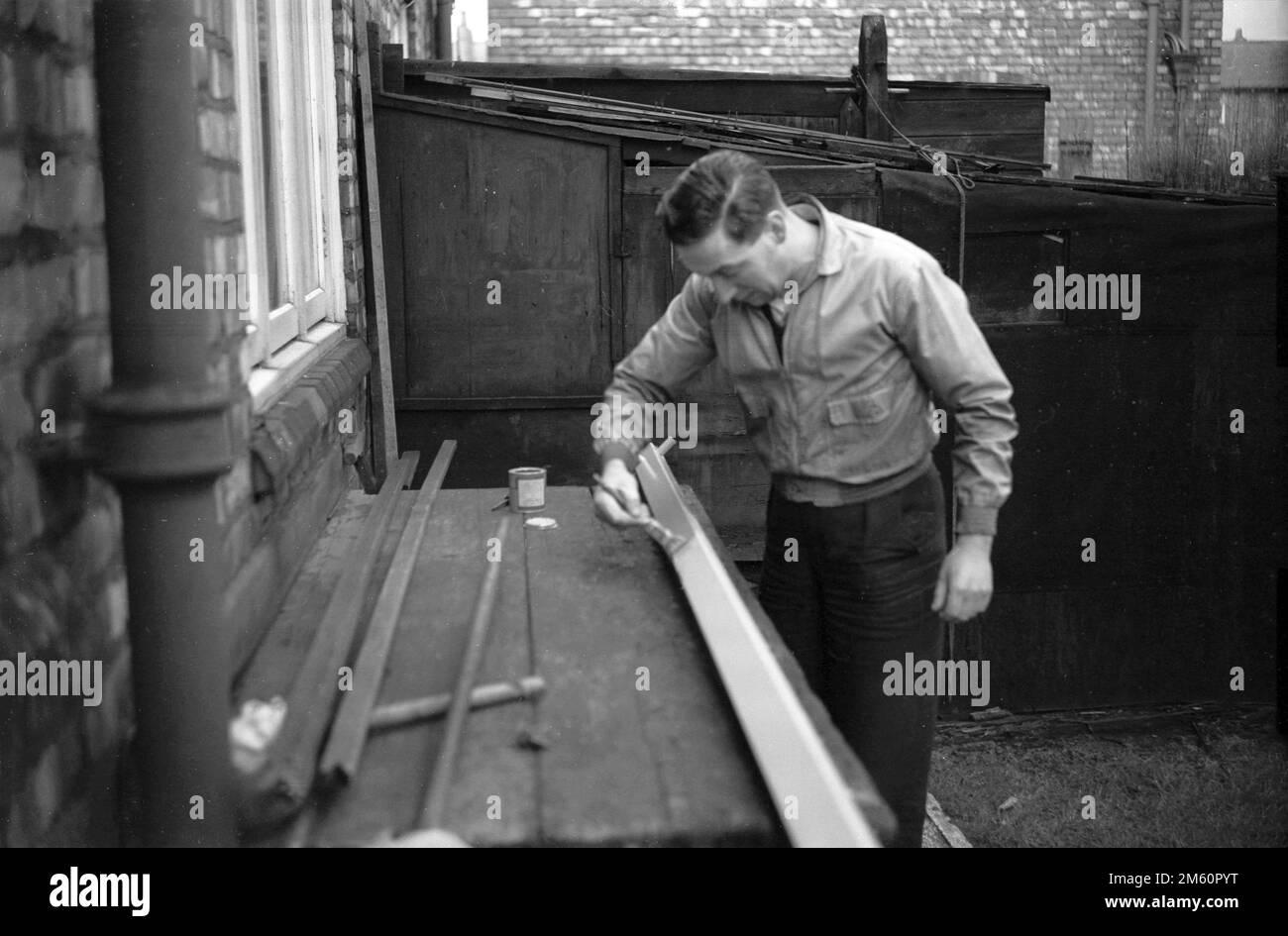 1950s, historical, on a bench in the backyard of a house, a man painting a piece of wood. Stock Photo