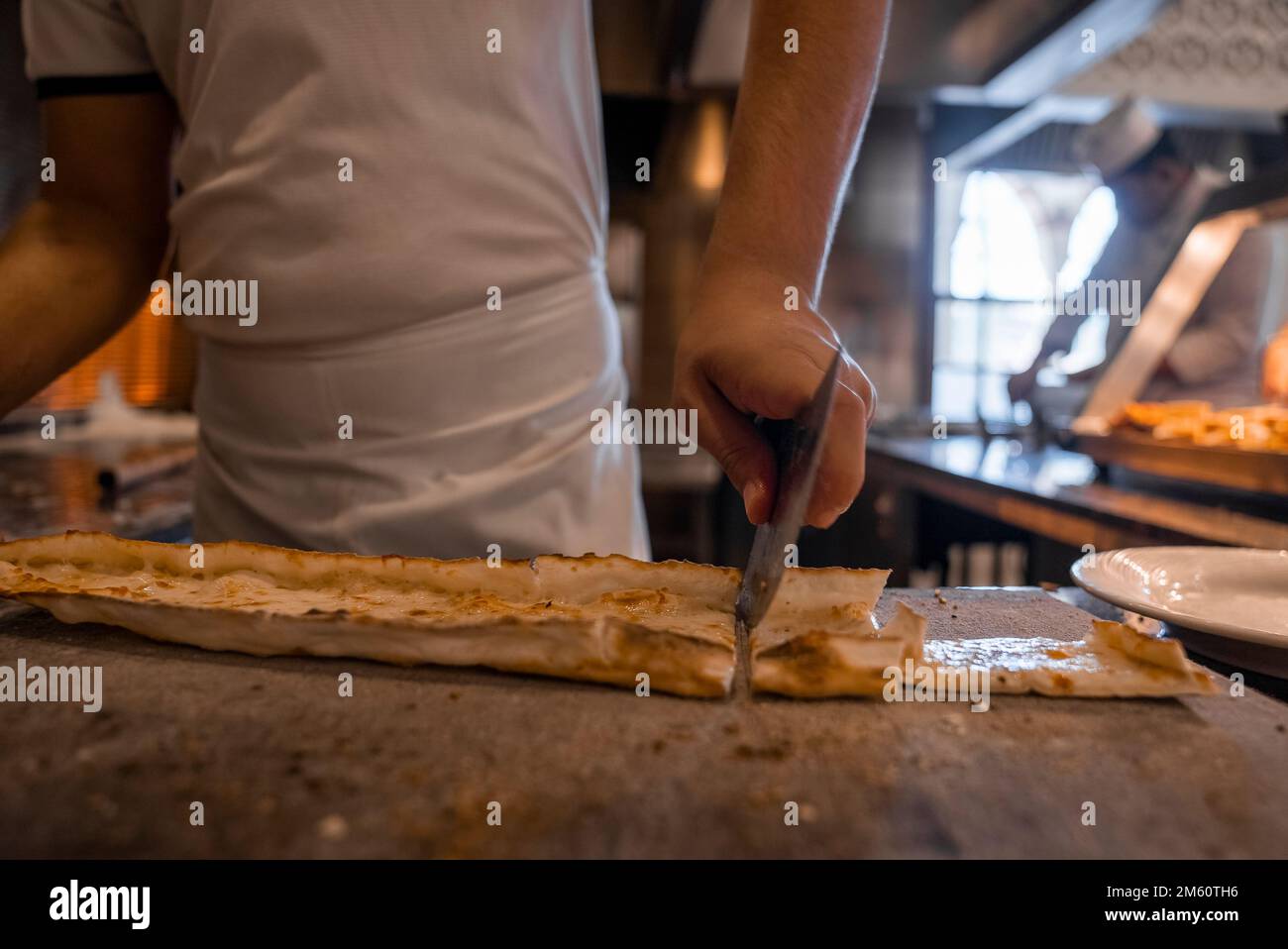Chef cutting Turkish cheese pide into slices on table at restaurant Stock Photo