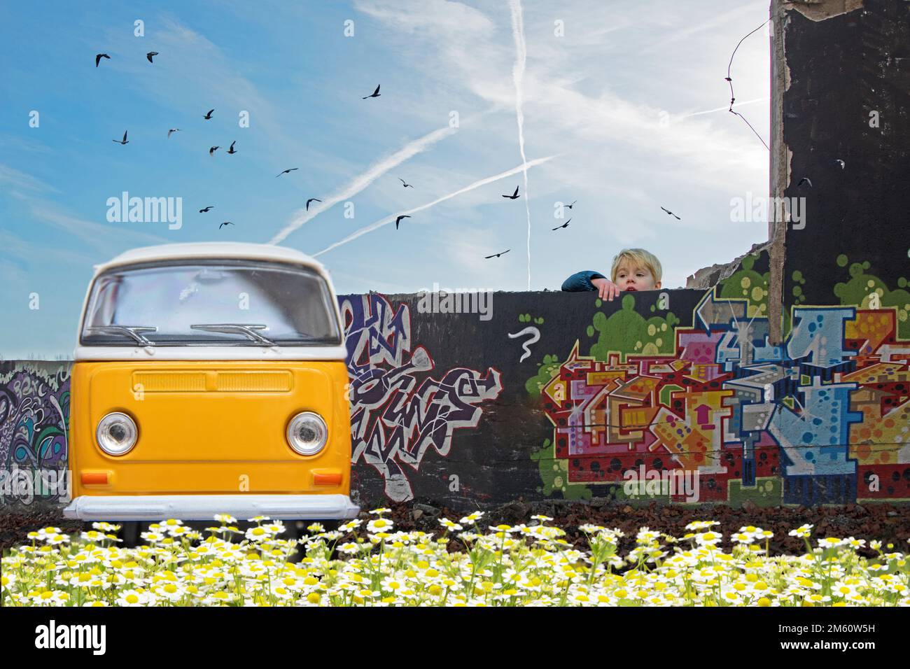 Young boy climbing the wall to see the yellow old car parked in the front of a graffiti wall Stock Photo