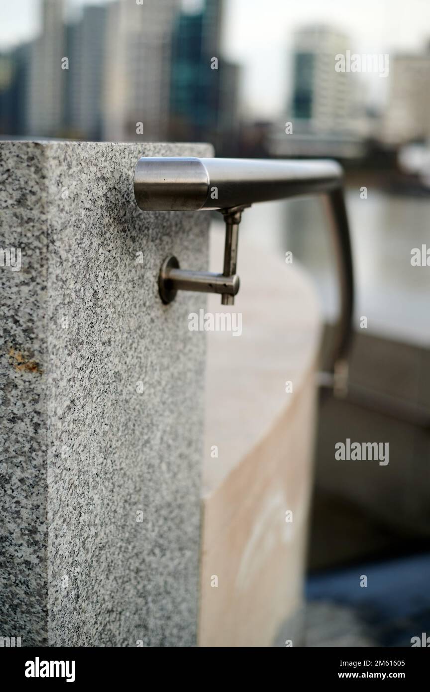 Metal hand railing with water drops against grey marble block in built up urban setting with background blur of buildings Stock Photo