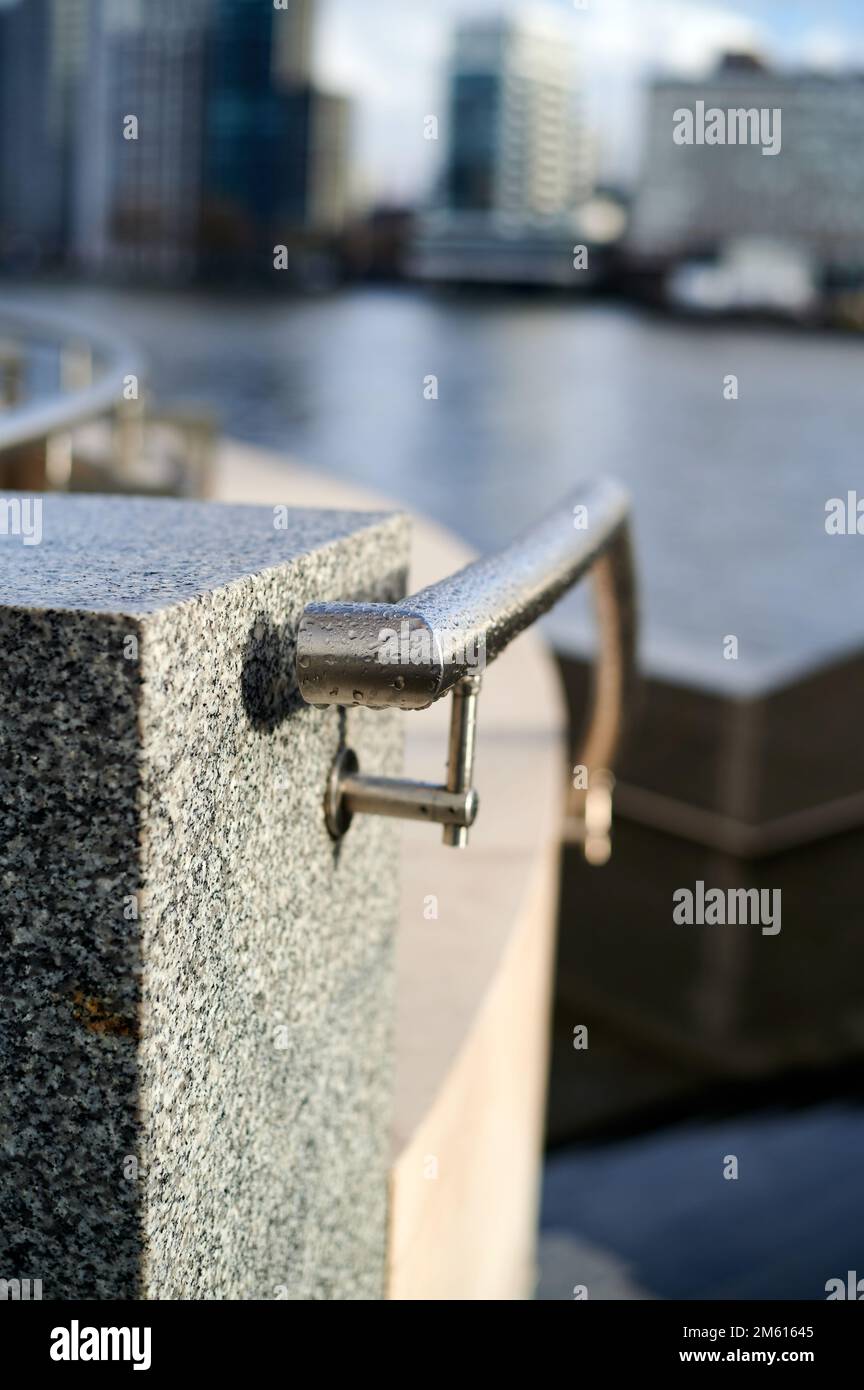 Metal hand railing with water drops against grey marble block in built up urban setting with background blur of buildings and river Stock Photo