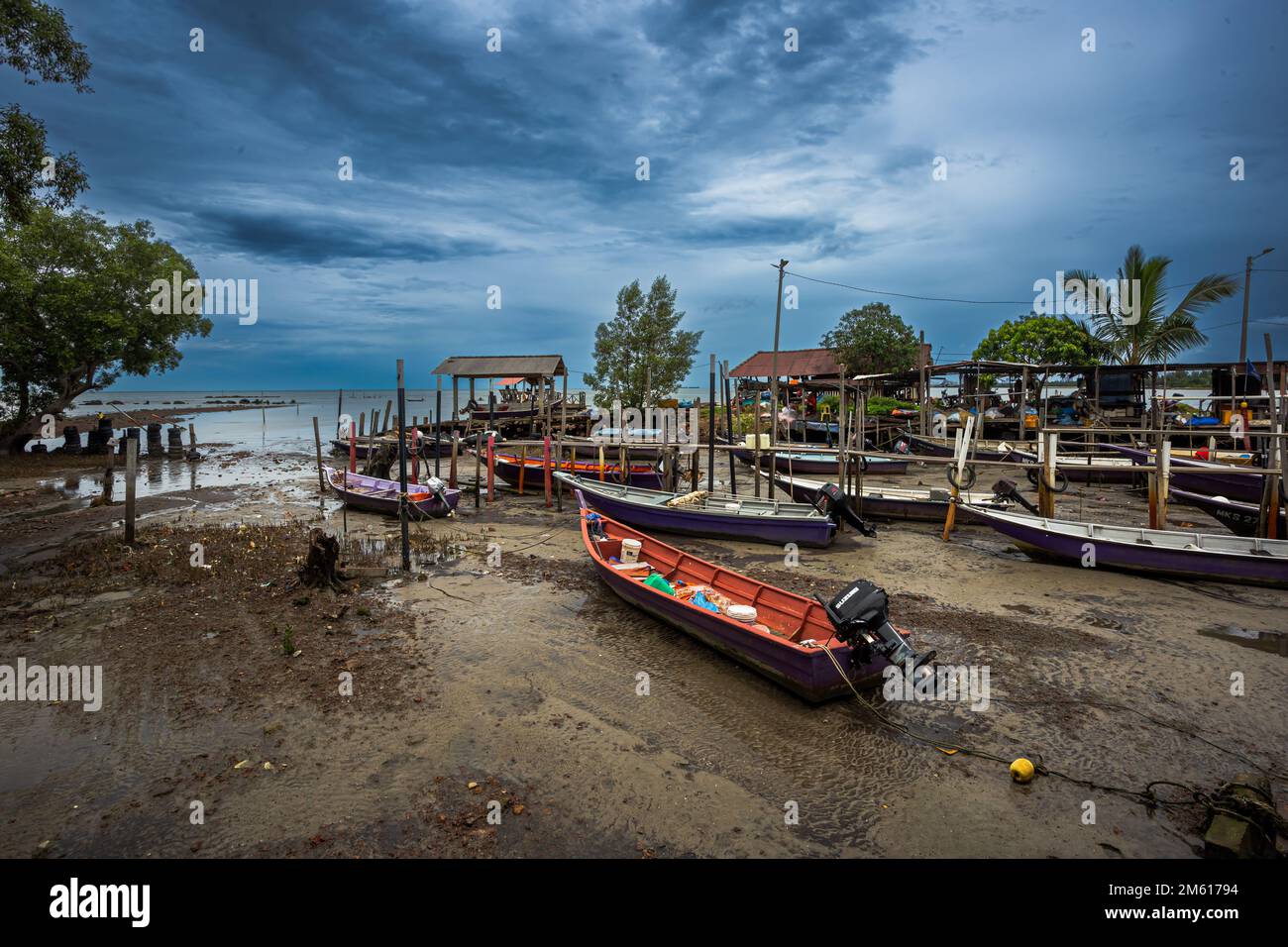 At low tide, fishing boats stand on the ground in a dry beach of a small fishing village in Malacca or Melaka, Peninsular Malaysia. Stock Photo