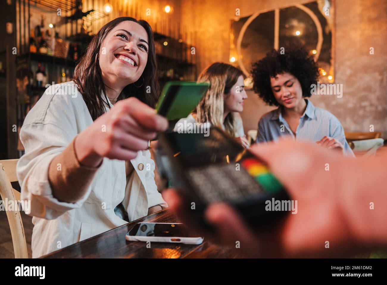 Happy young woman paying bill with a contactless credit card in a restaurant. Female smiling holding a creditcard and giving a payment transaction to the cashier. High quality photo Stock Photo